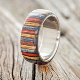 Shown here is "Haven", a custom, handcrafted men's wedding ring featuring a birch wood overlay that has been dyed red, grey, and brown, upright facing left. Additional overlay options are available upon request.
