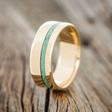Shown here is "Vertigo", a custom, handcrafted men's wedding ring featuring a 14K gold wedding band with a malachite inlay, upright facing left. Additional inlay options are available upon request.