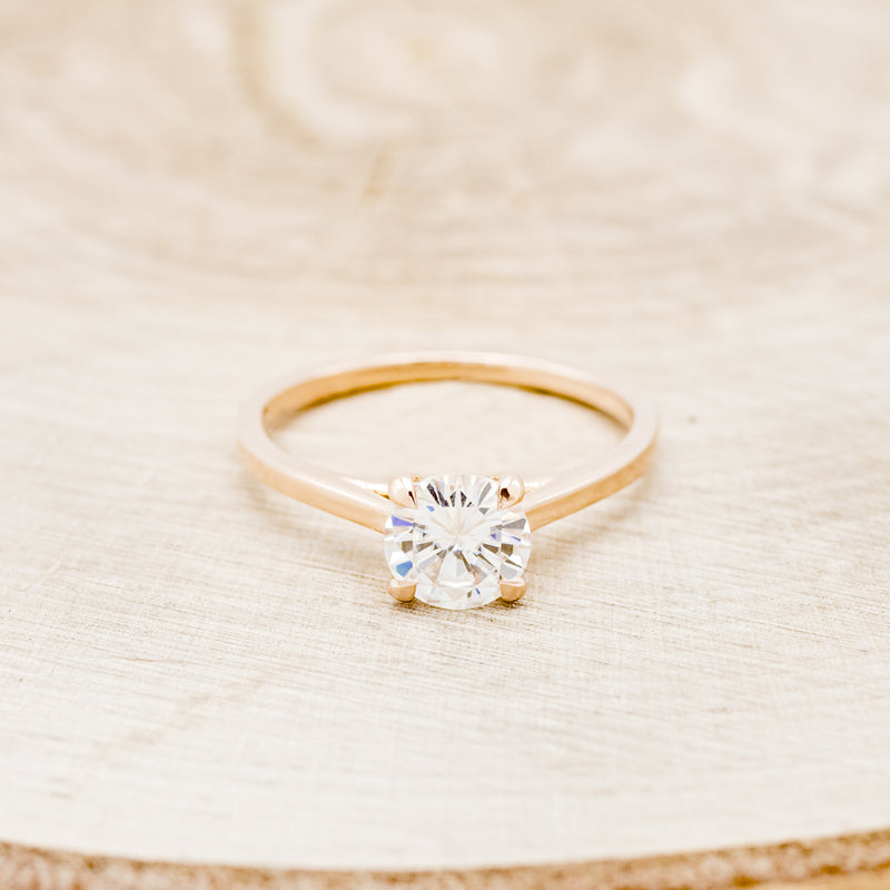 Shown here is a solitaire-style moissanite women's engagement ring with 4 claw prongs, front facing. Many other center stone options are available upon request.