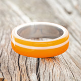 Shown here is "Remmy", a custom, handcrafted men's wedding ring featuring a hand-turned orange & white acrylic, laying flat. Additional inlay options are available upon request.