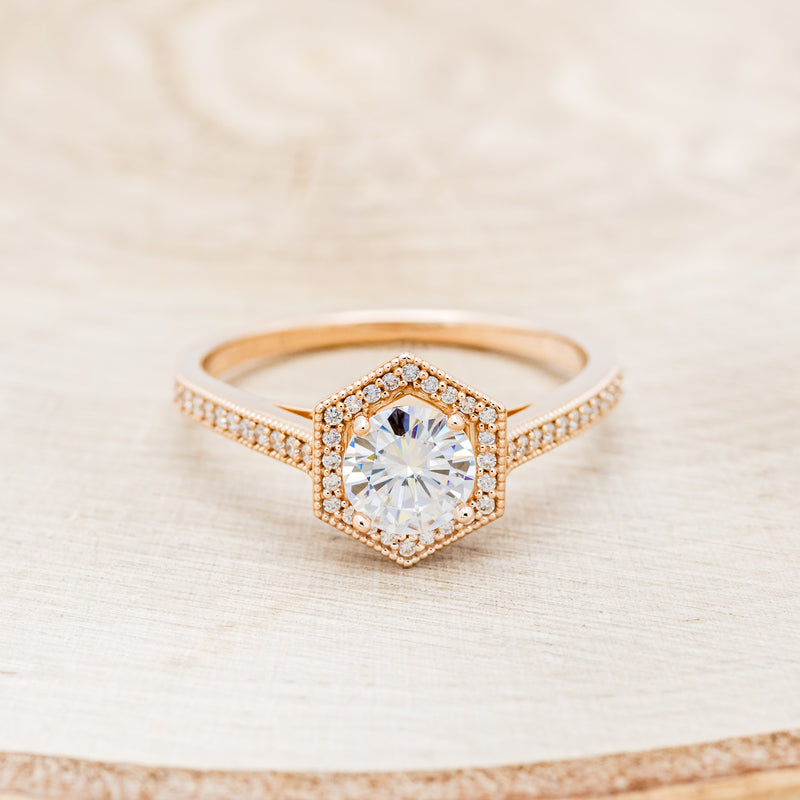 Shown here is "Odessa", a geometric-style moissanite women's engagement ring with a diamond halo and diamond accents, front facing. Many other center stone options are available upon request.