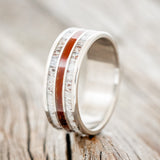 Shown here is "Rio", a custom, handcrafted men's wedding ring featuring 3 channels with elk antler and padauk wood inlays on a titanium band, upright facing left. Additional inlay options are available upon request.