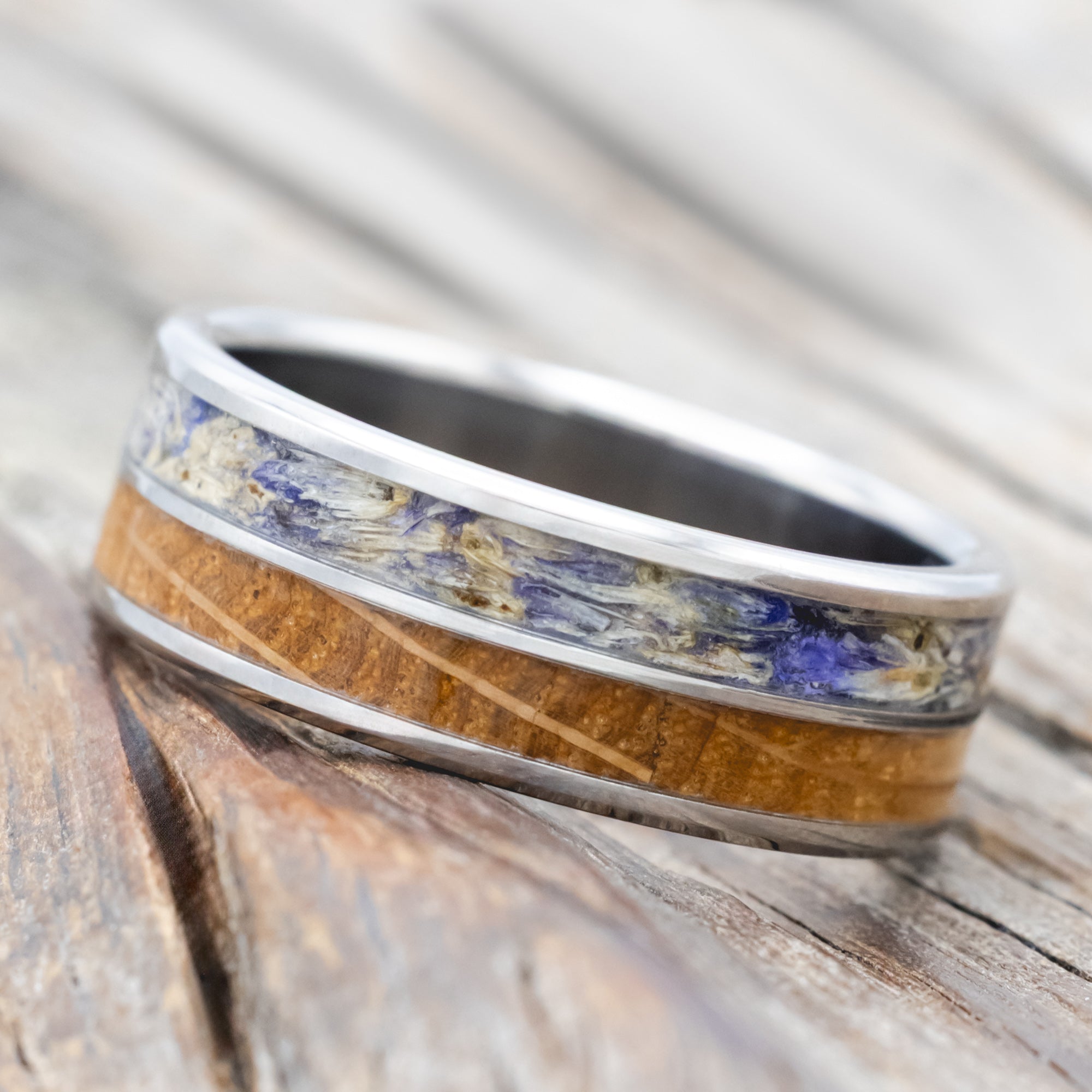 Titanium ring with whiskey barrel oak and bluebell inlay on a wooden surface