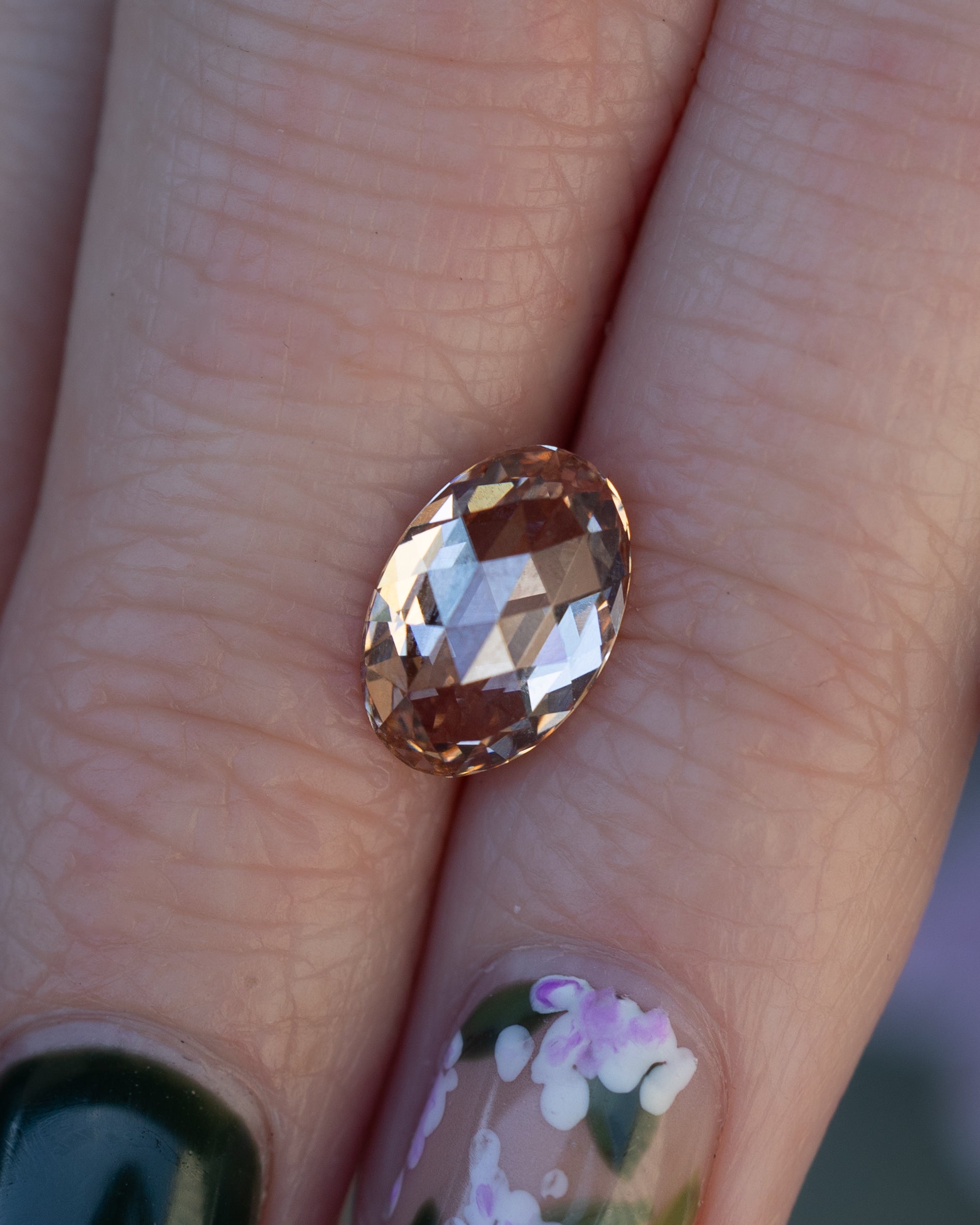 Close up of fingers holding an oval champagne diamond.