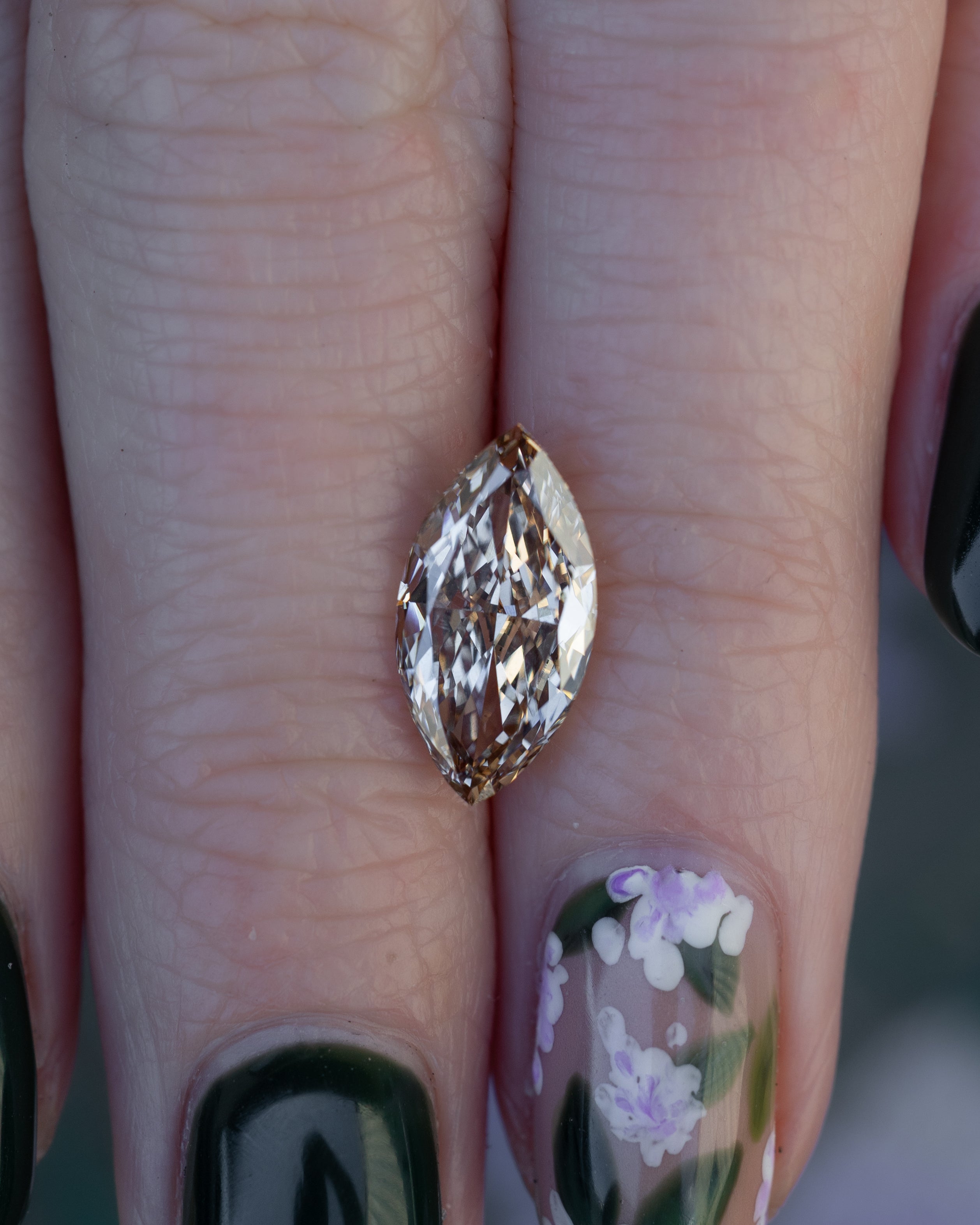 Close up of hand holding a champagne diamond against a floral background