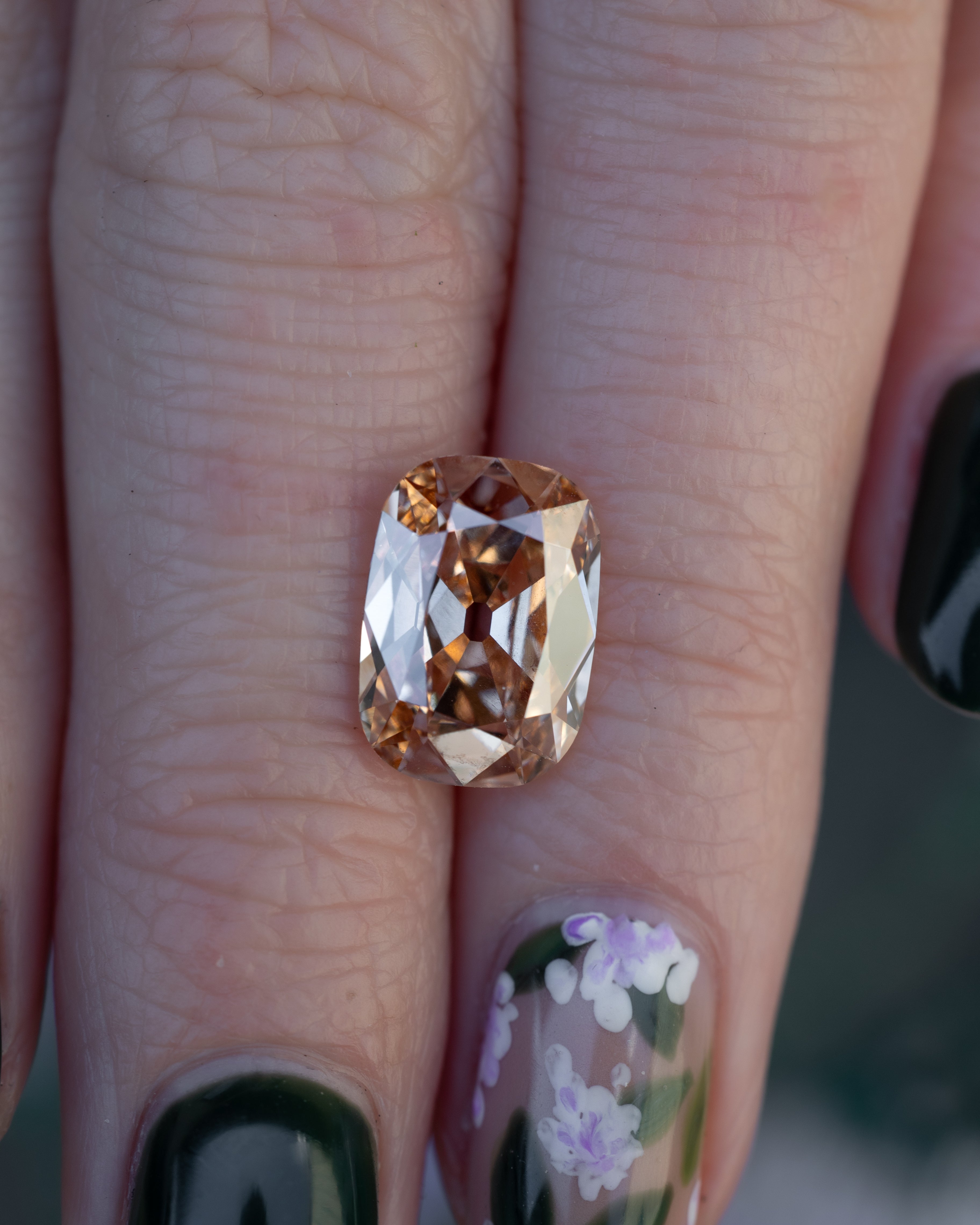 Hand holding champagne diamond against a floral background