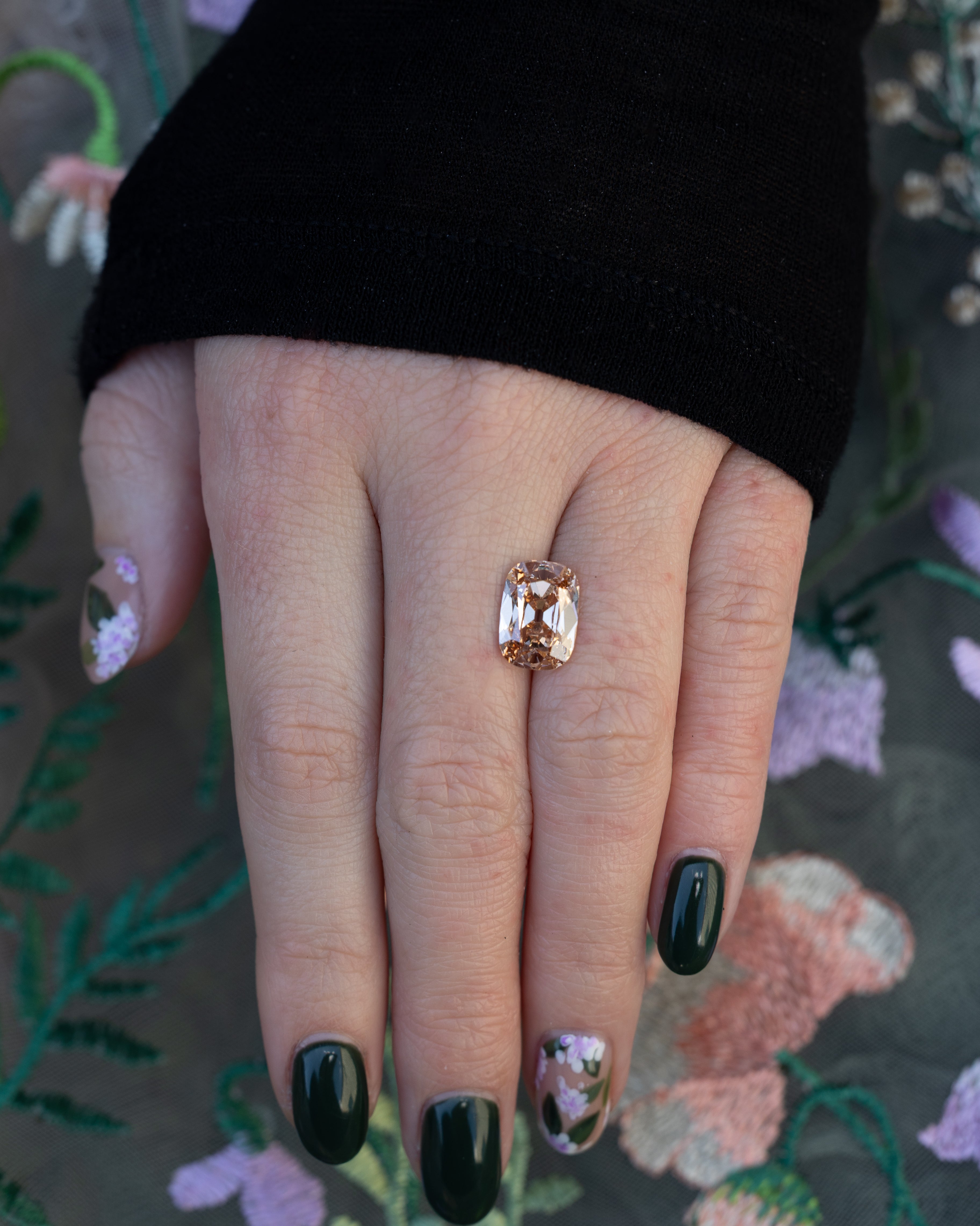 Hand holding a champagne diamond against a floral background