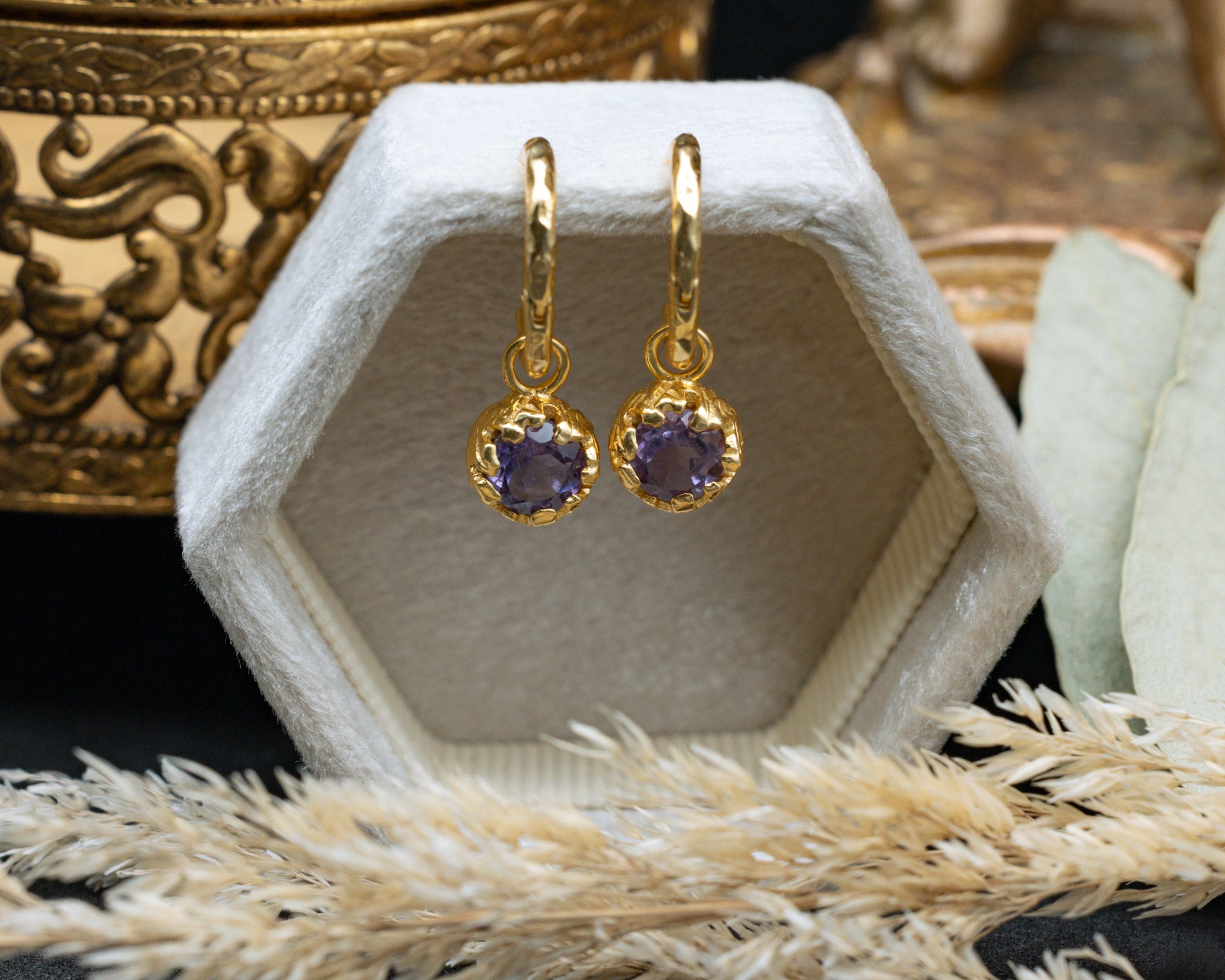 Gold earrings with purple amethyst on a decorative stand.