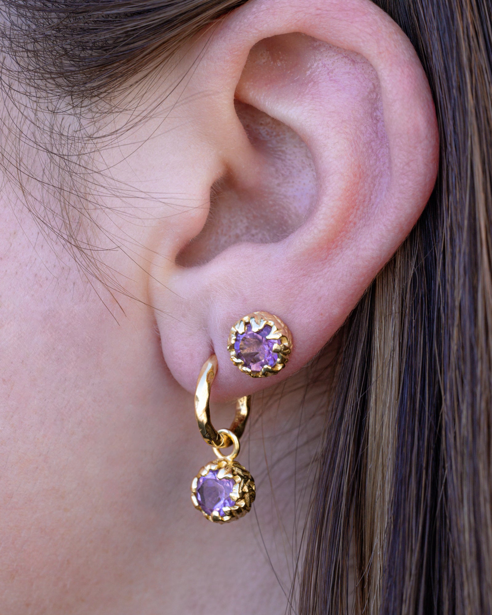 Close-up of an ear wearing gold earrings with purple amethyst.