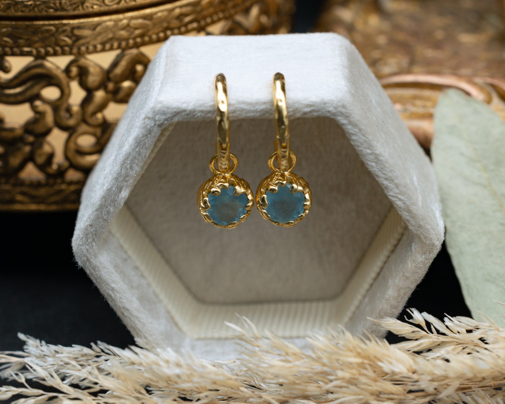 Gold earrings with aquamarine on a white hexagonal stand with decorative background