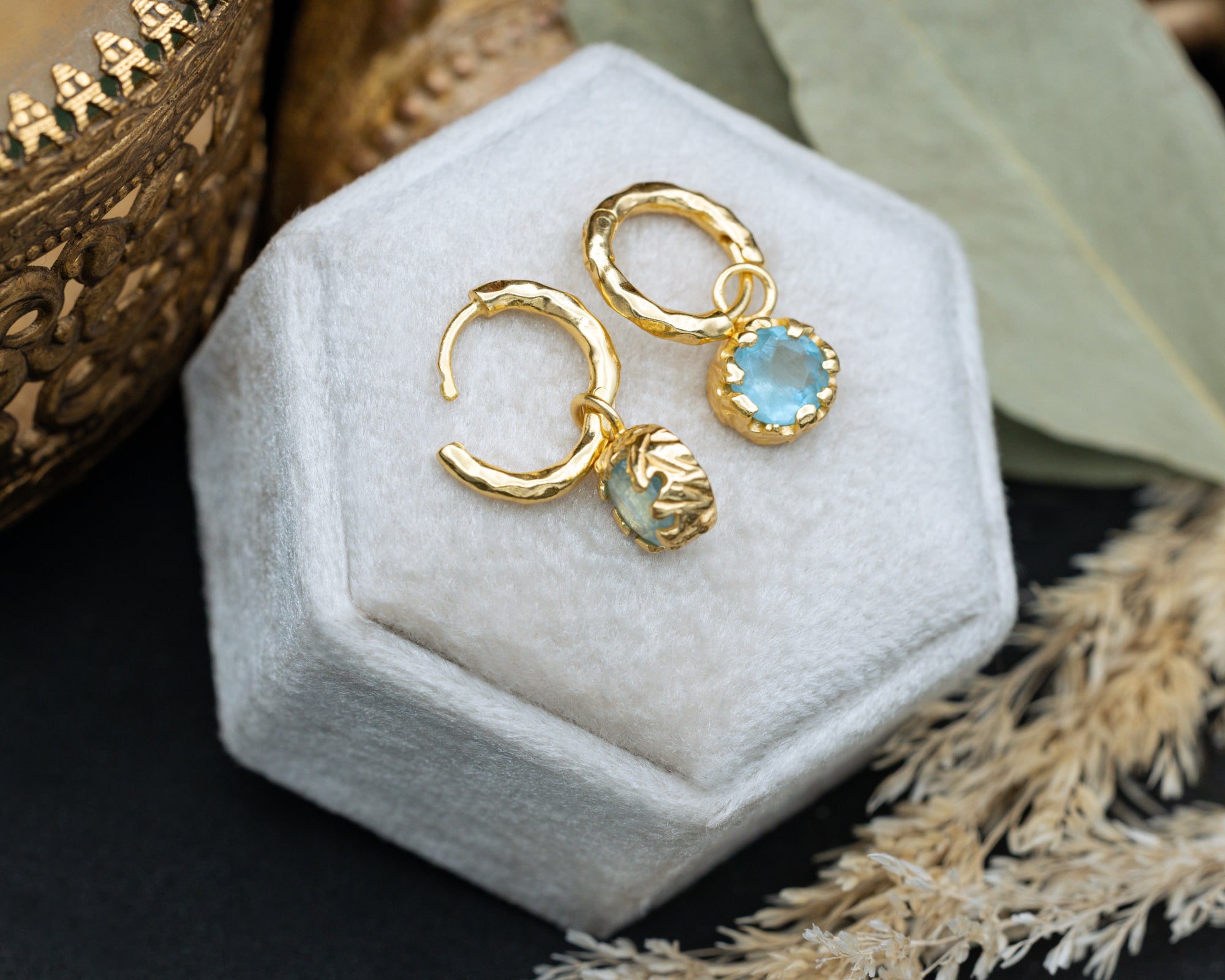 Gold hoop earrings with aquamarine on a white jewelry box