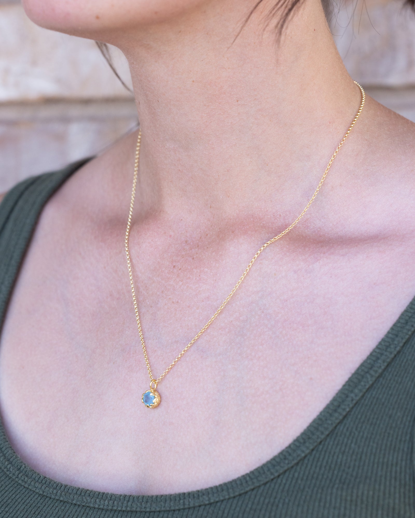 Gold necklace with an aquamarine pendant worn by a person in a green top.