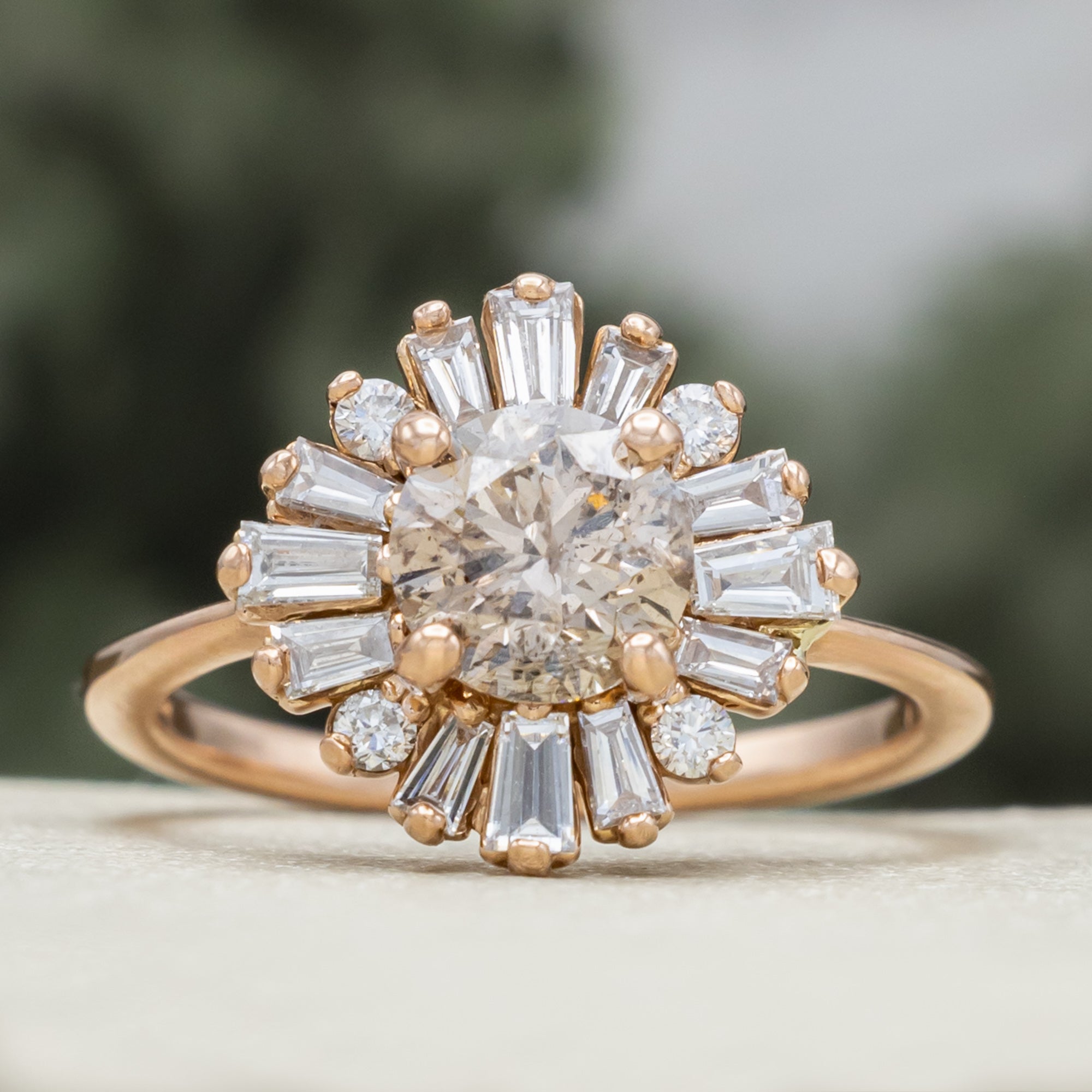 Rose gold champagne diamond engagement ring with diamond halo against a blurred green background