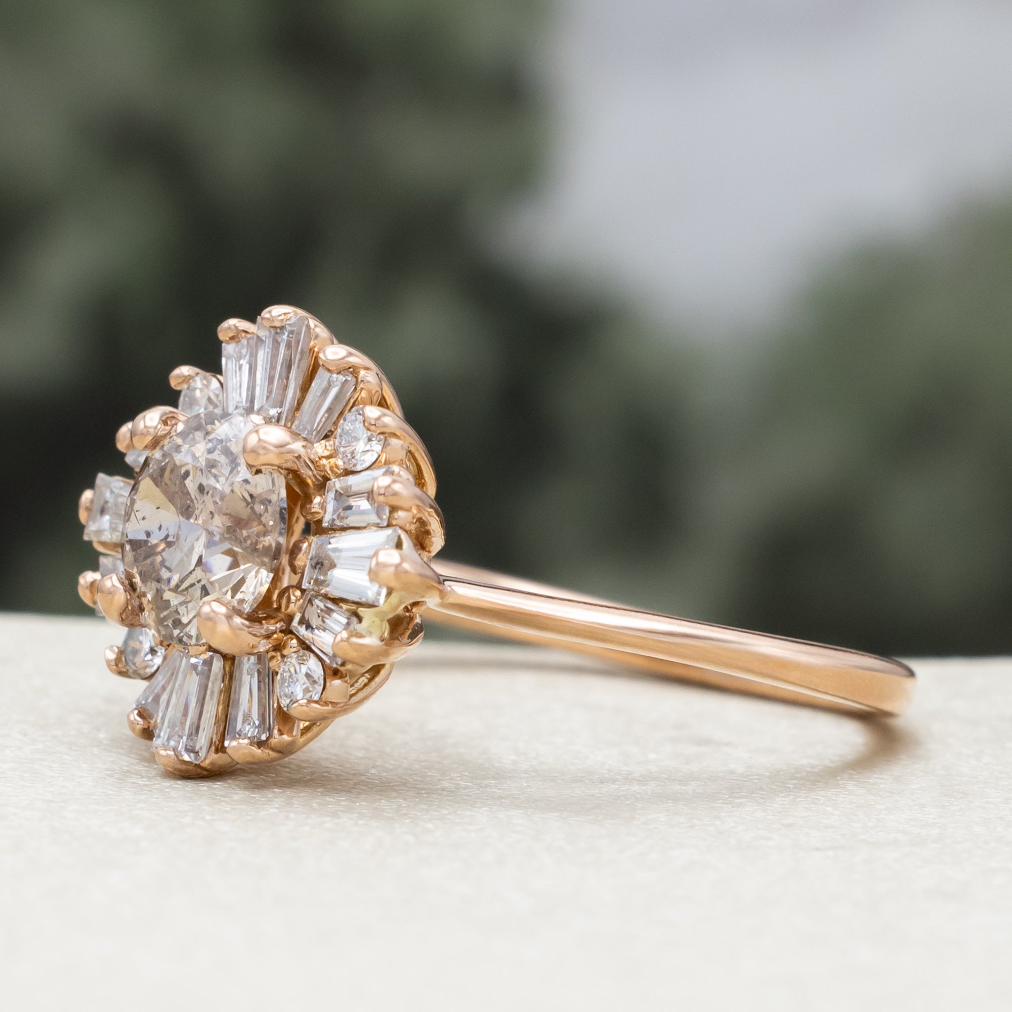Rose gold champagne diamond engagement ring with diamond halo against a blurred green background