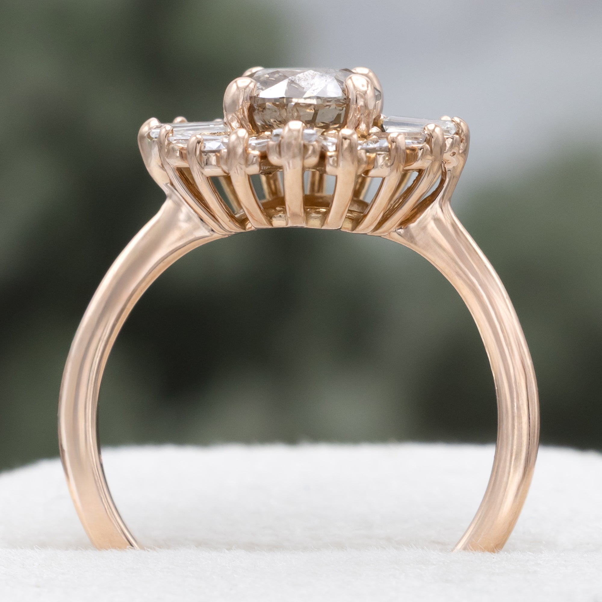 Rose gold champagne diamond engagement ring with diamond halo against a blurred green background