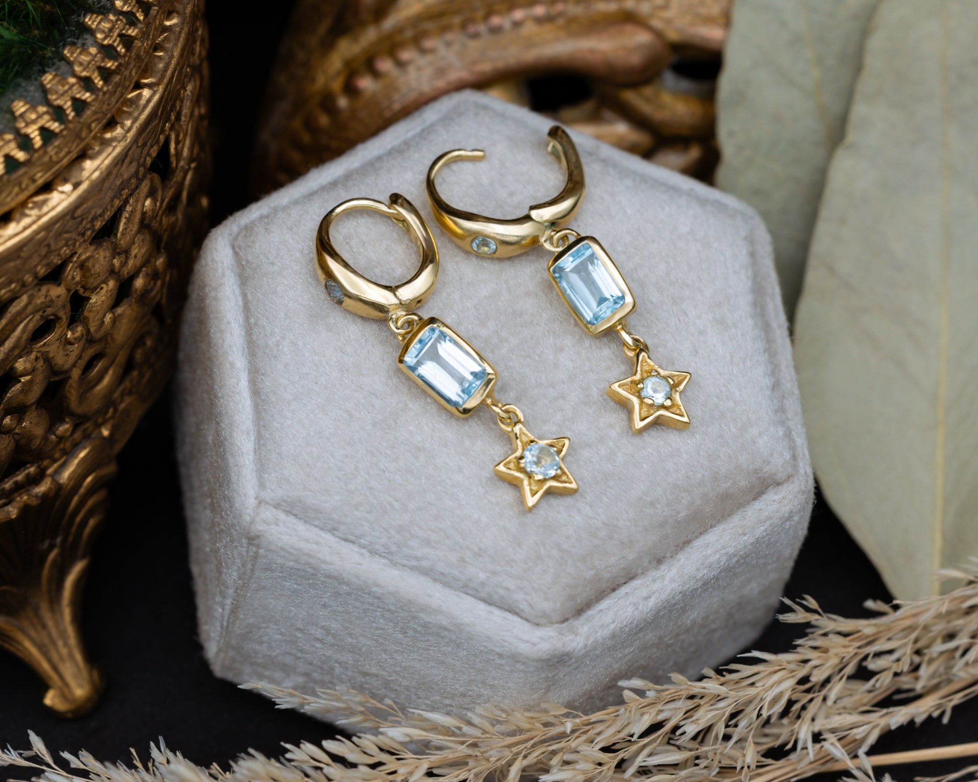Gold earrings with star and blue topaz gemstone accents on a decorative cushion