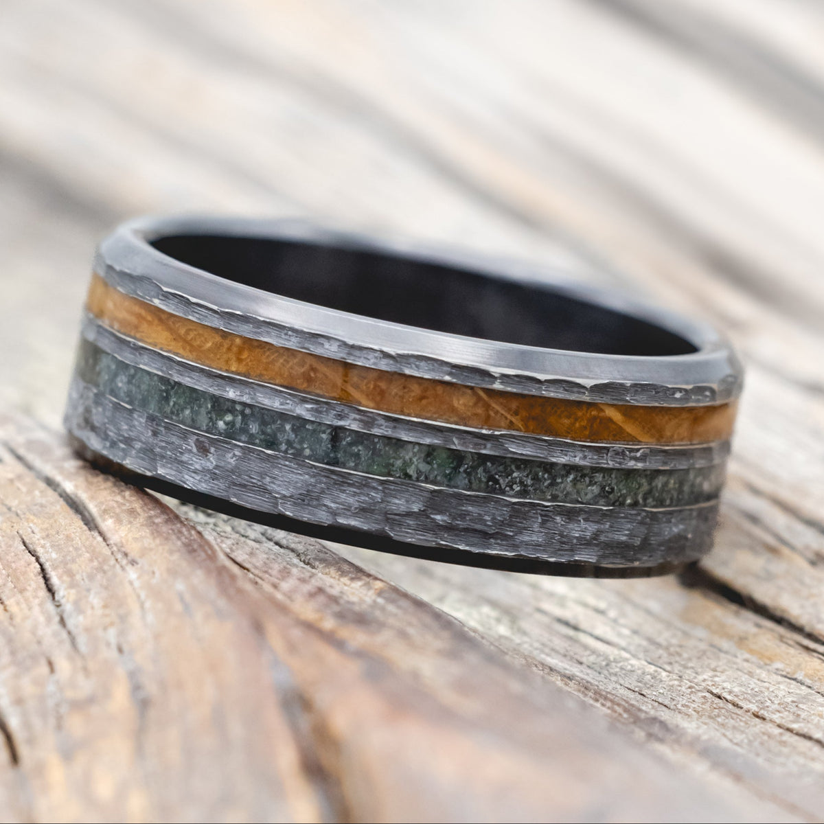 Black zirconium ring with whiskey barrel oak and moss agate on a wooden surface
