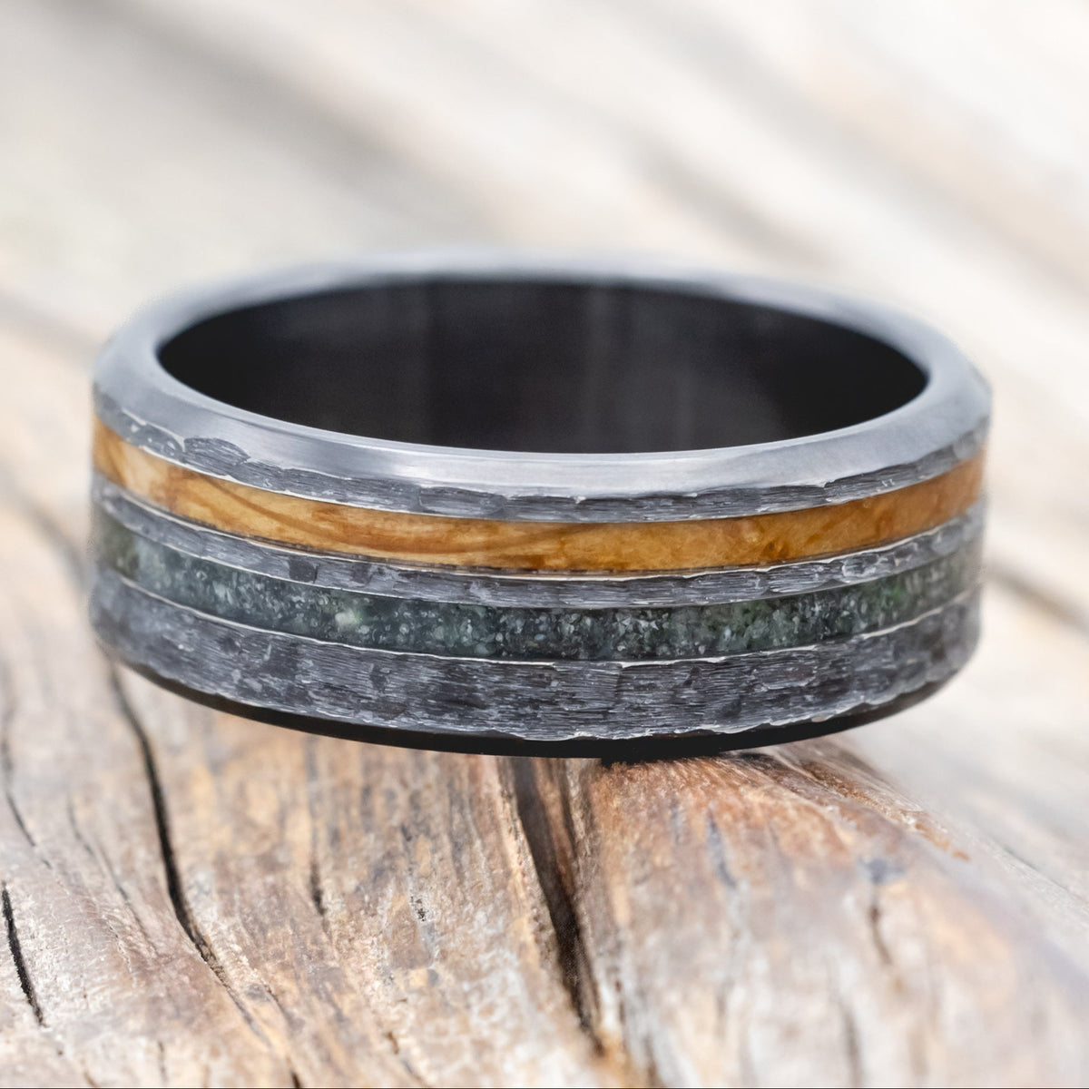 Black zirconium ring with whiskey barrel oak and moss agate on a wooden surface