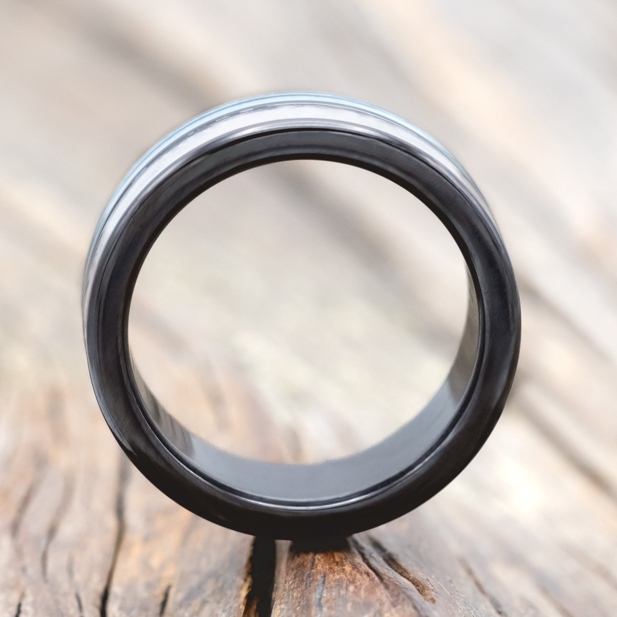 Close-up of a black ring with a metallic band on a wooden surface