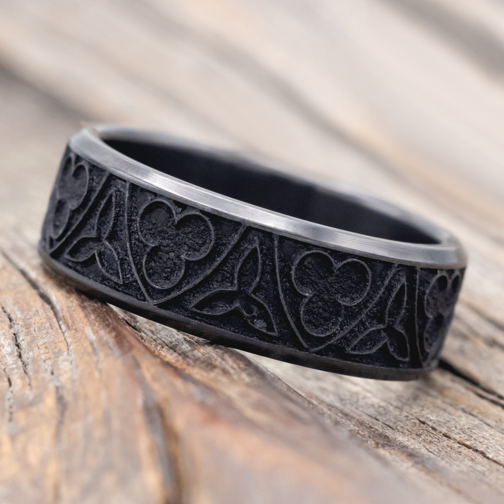 Black zirconium ring with intricate patterns on a wooden surface