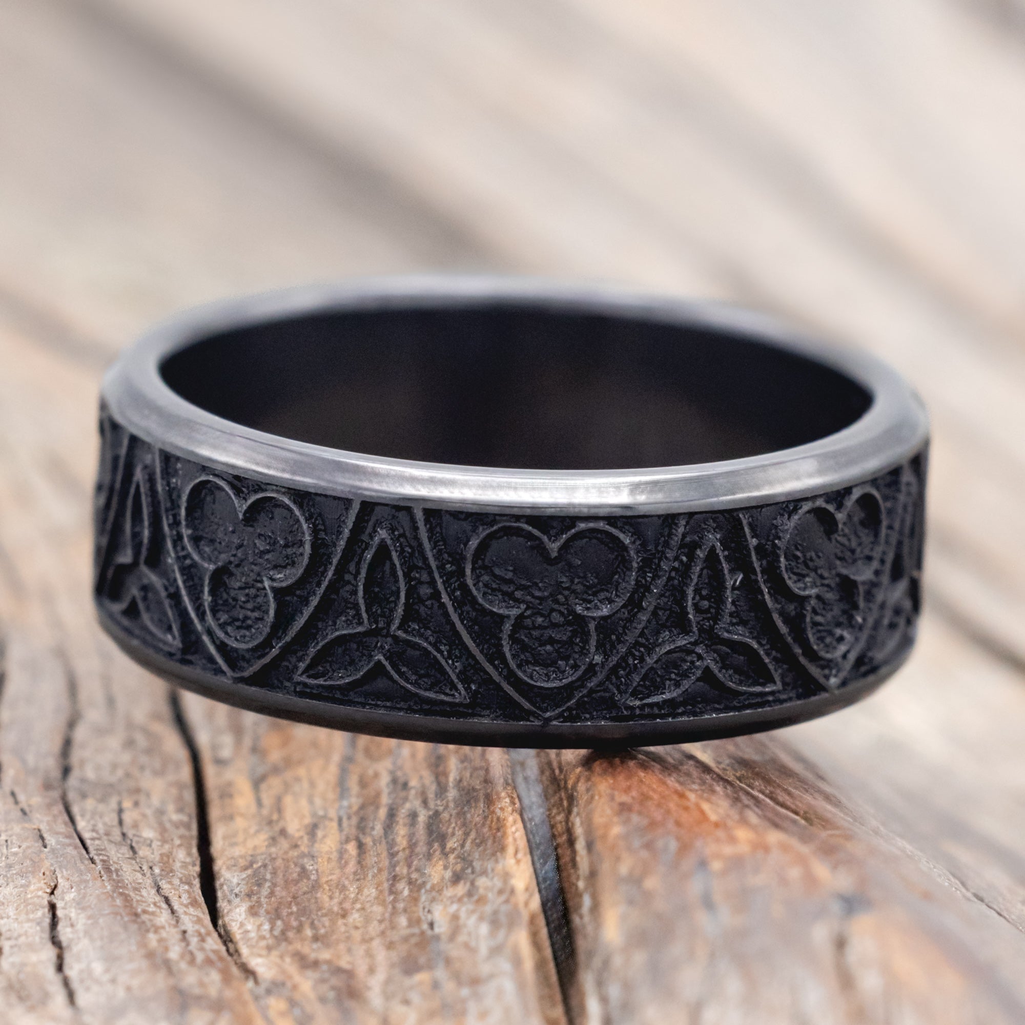 Black zirconium ring with intricate patterns on a wooden surface