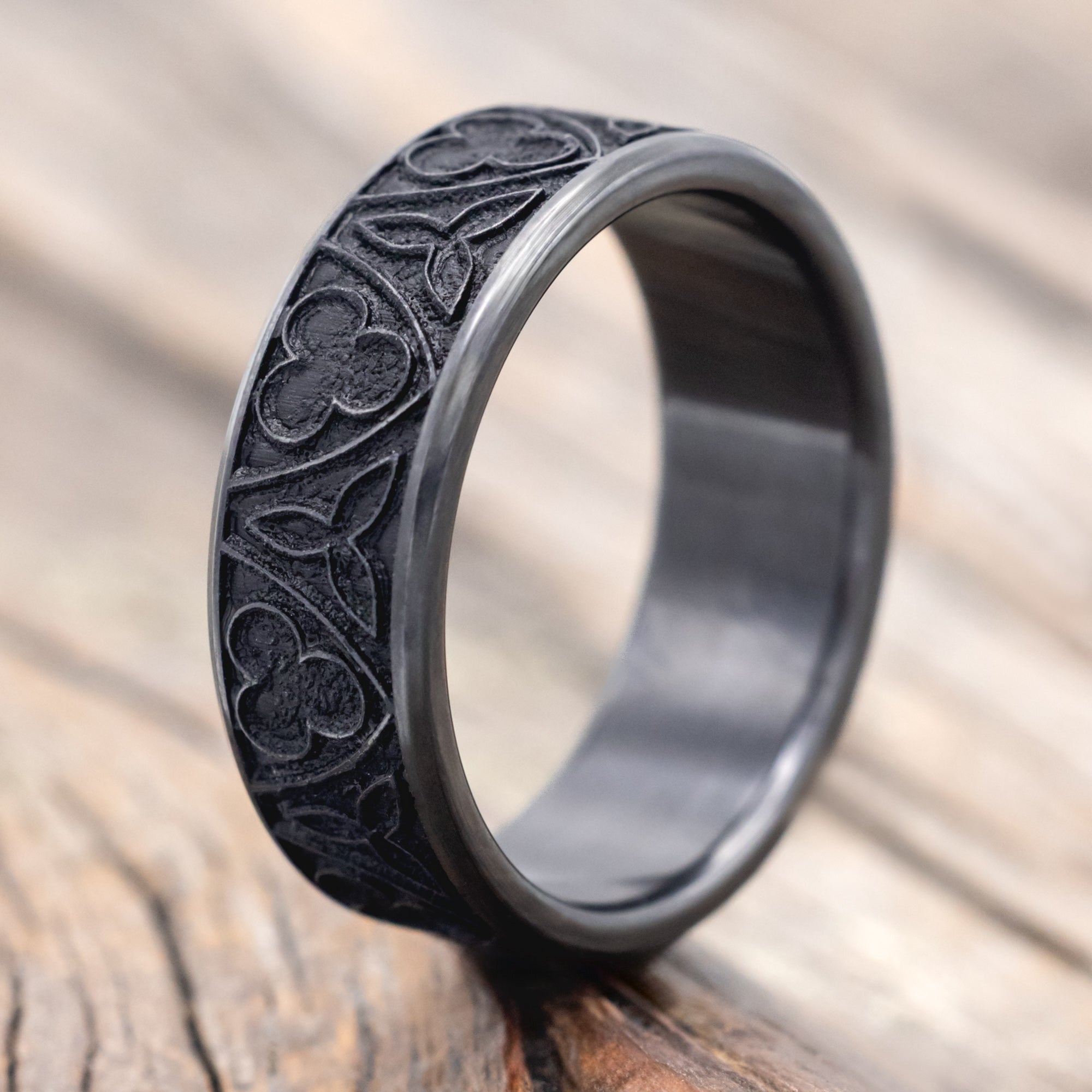 Black zirconium ring with intricate patterns on a wooden surface