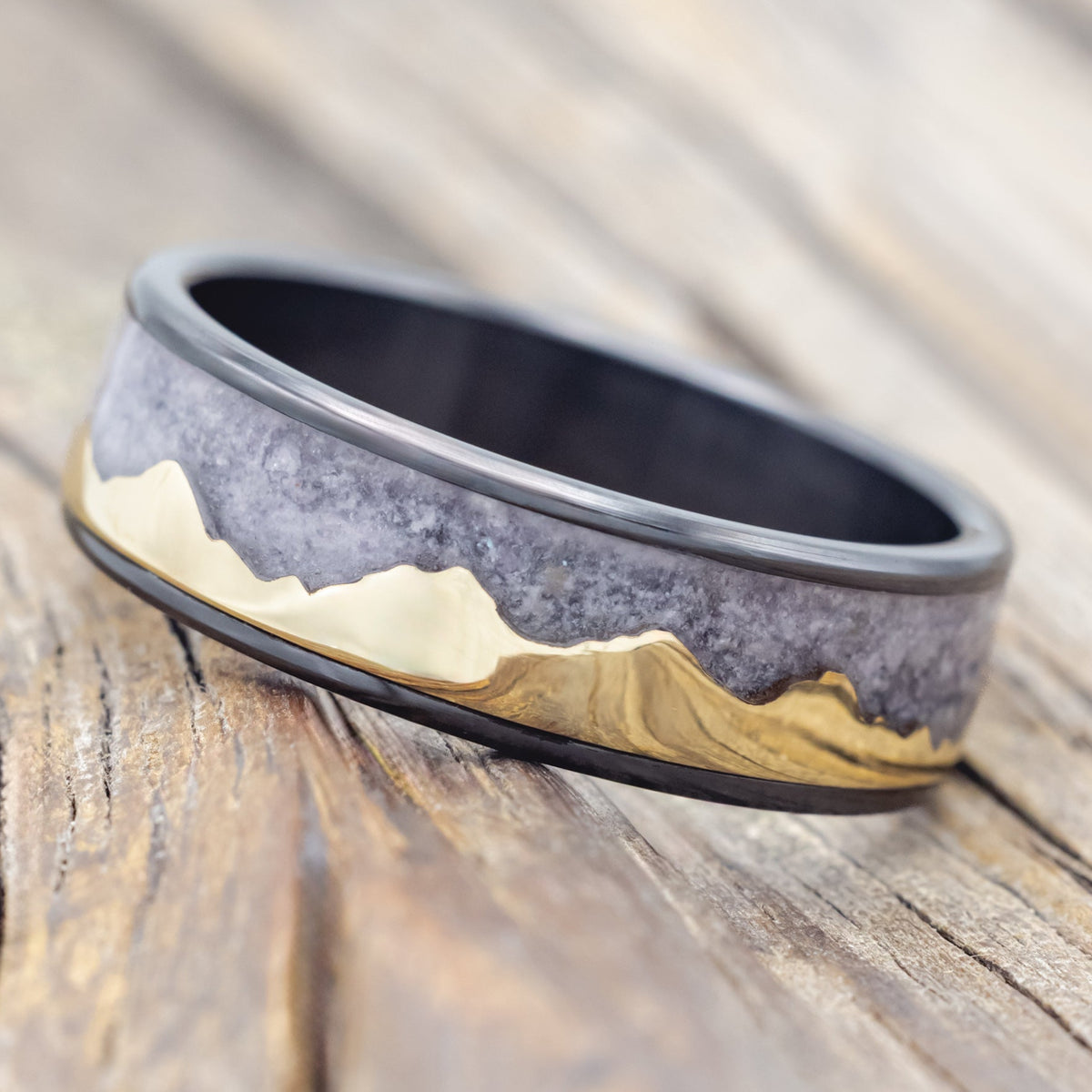 Black zirconium ring with 14K gold mountain design on a wooden surface
