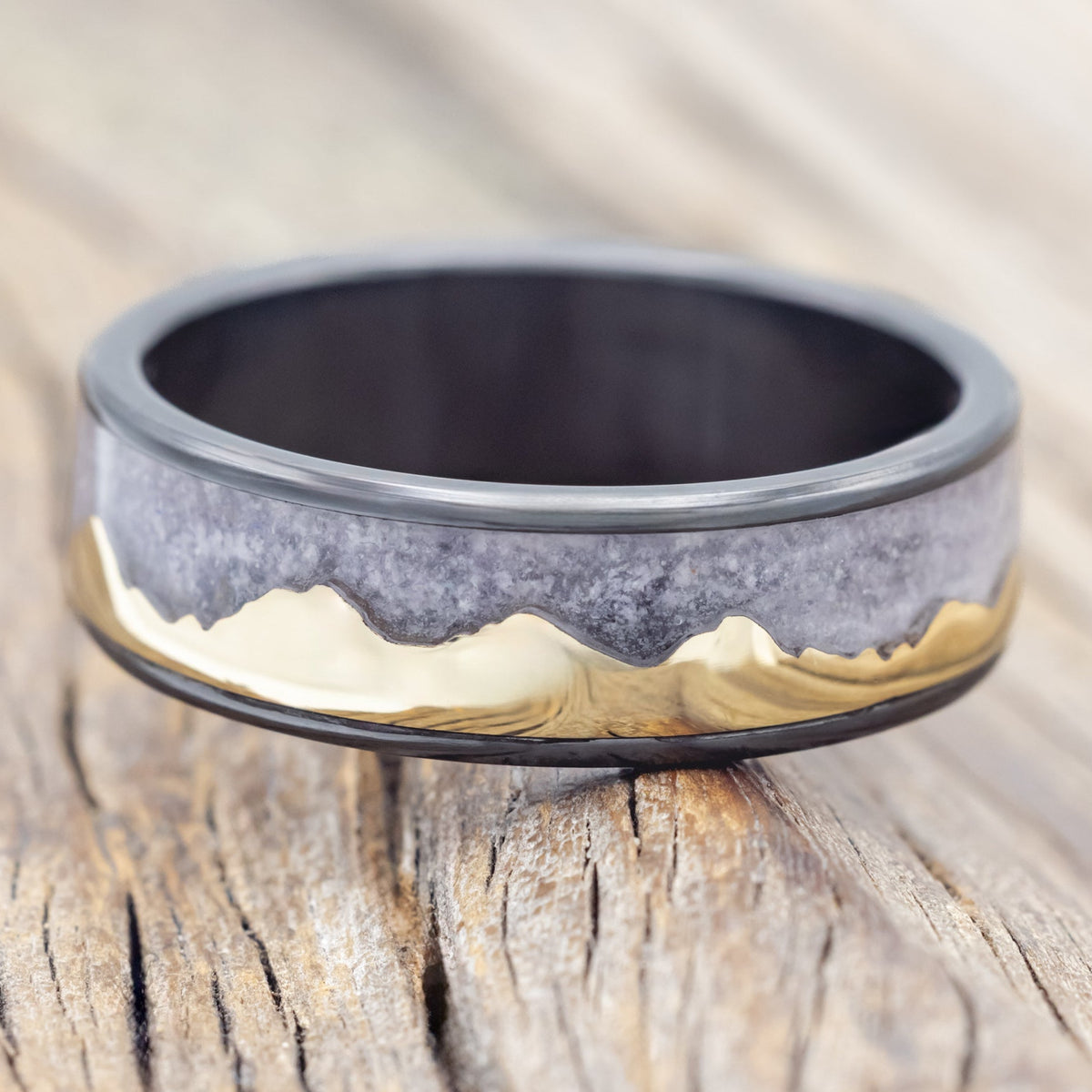 Black zirconium ring with 14K gold mountain design on a wooden surface