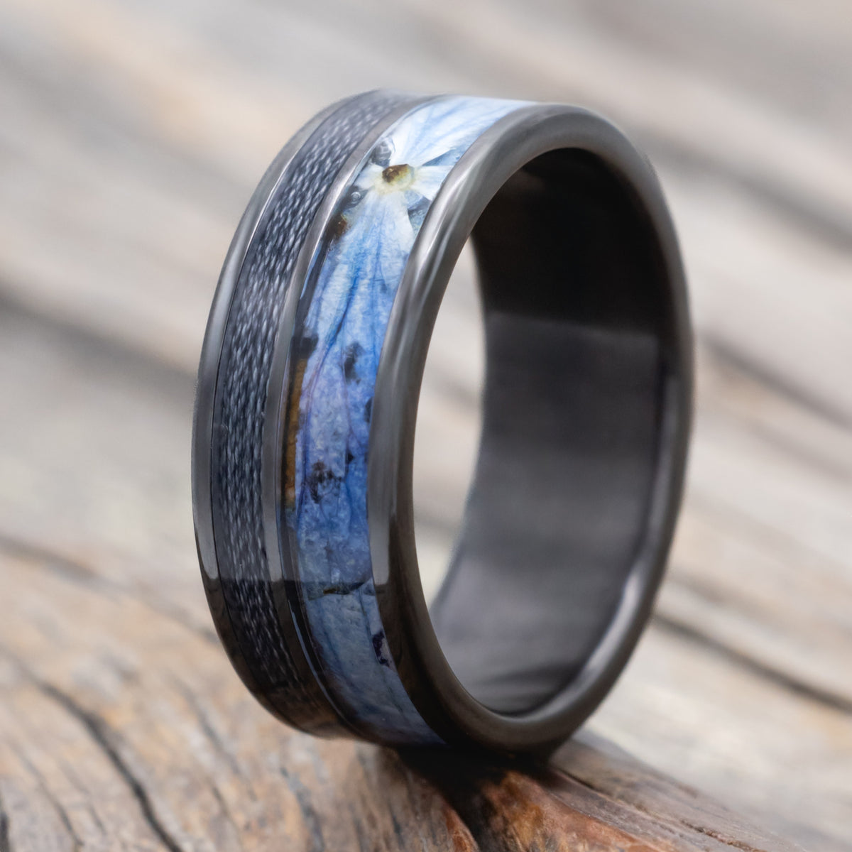 A black zirconium ring with fishing line and blue hydrangea inlays on a blurred wooden surface