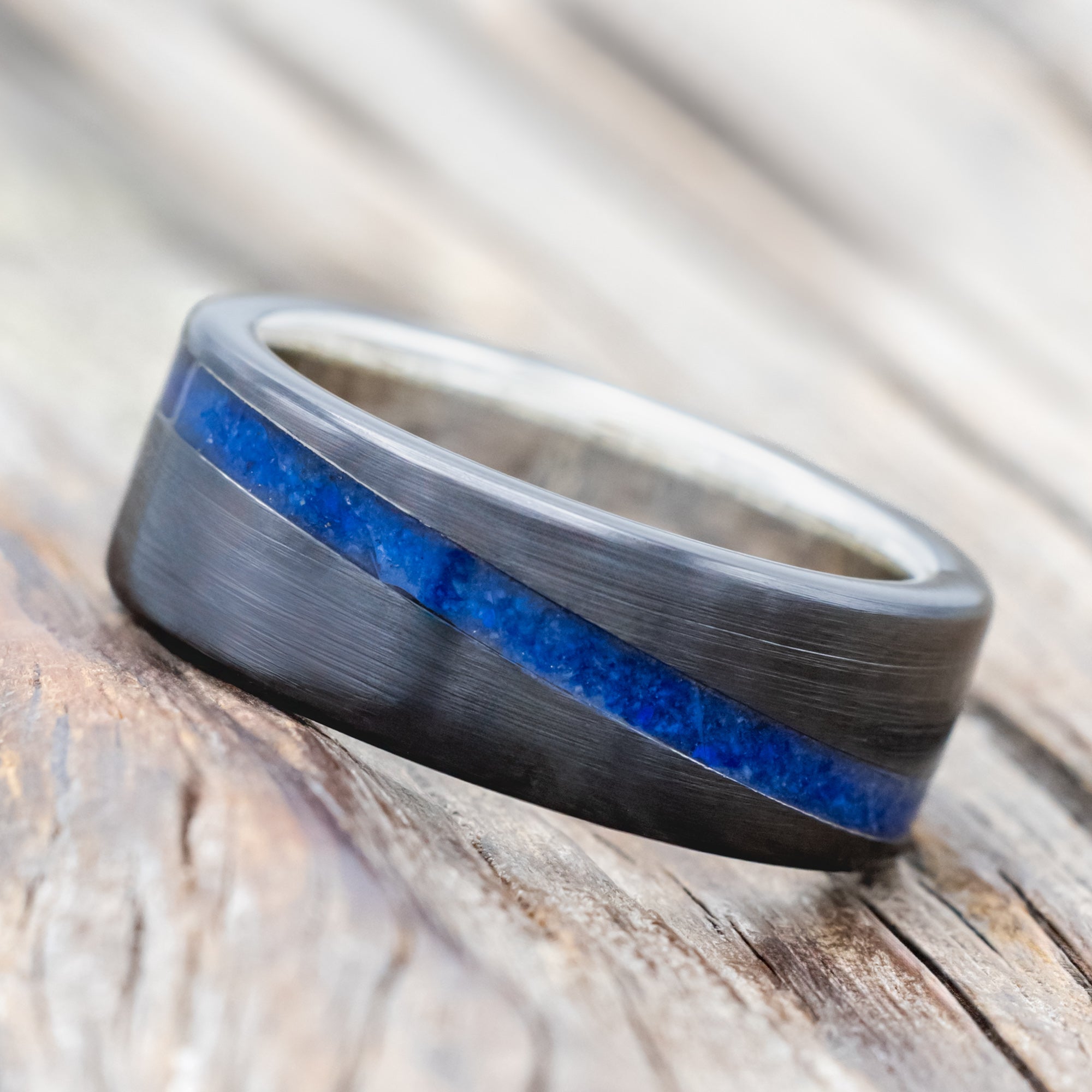 Black zirconium ring with lapis lazuli inlay and silver lining on a wooden surface