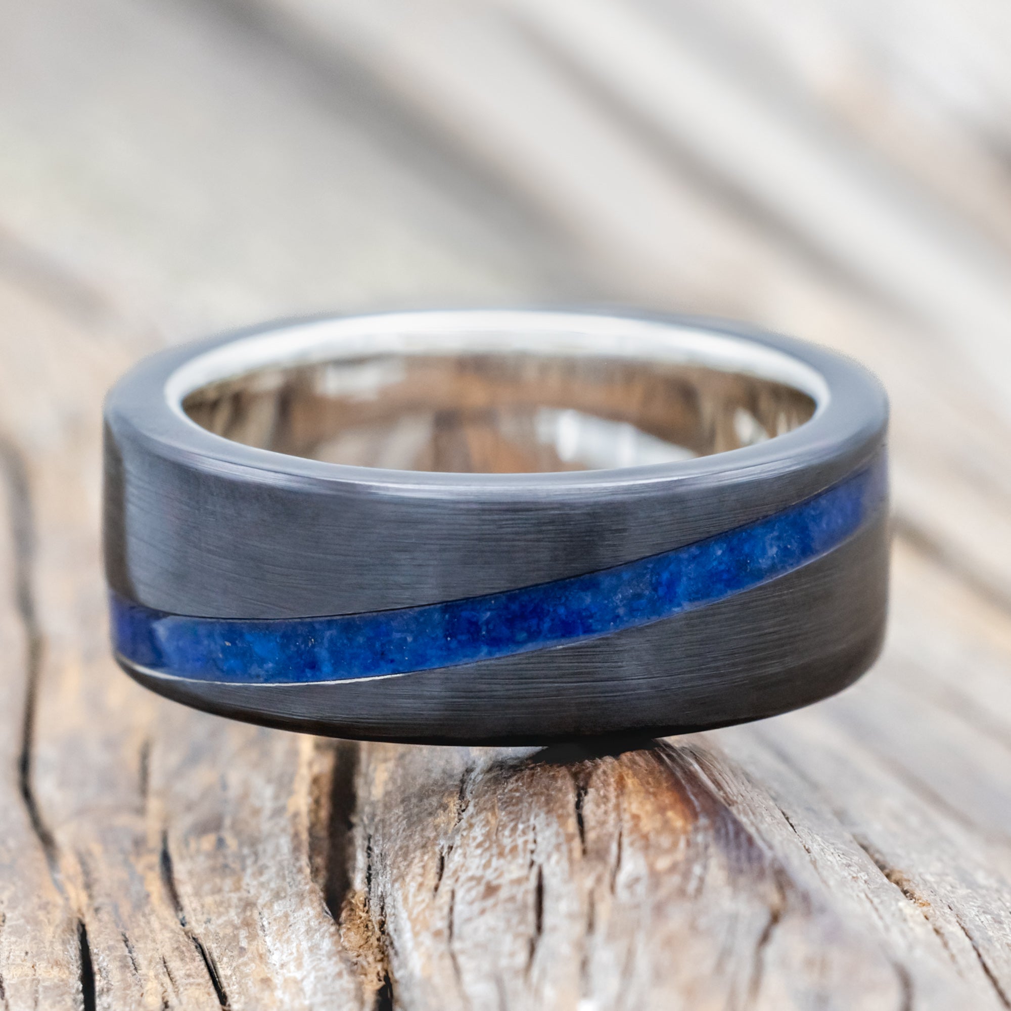 Black zirconium ring with lapis lazuli inlay and silver lining on a wooden surface