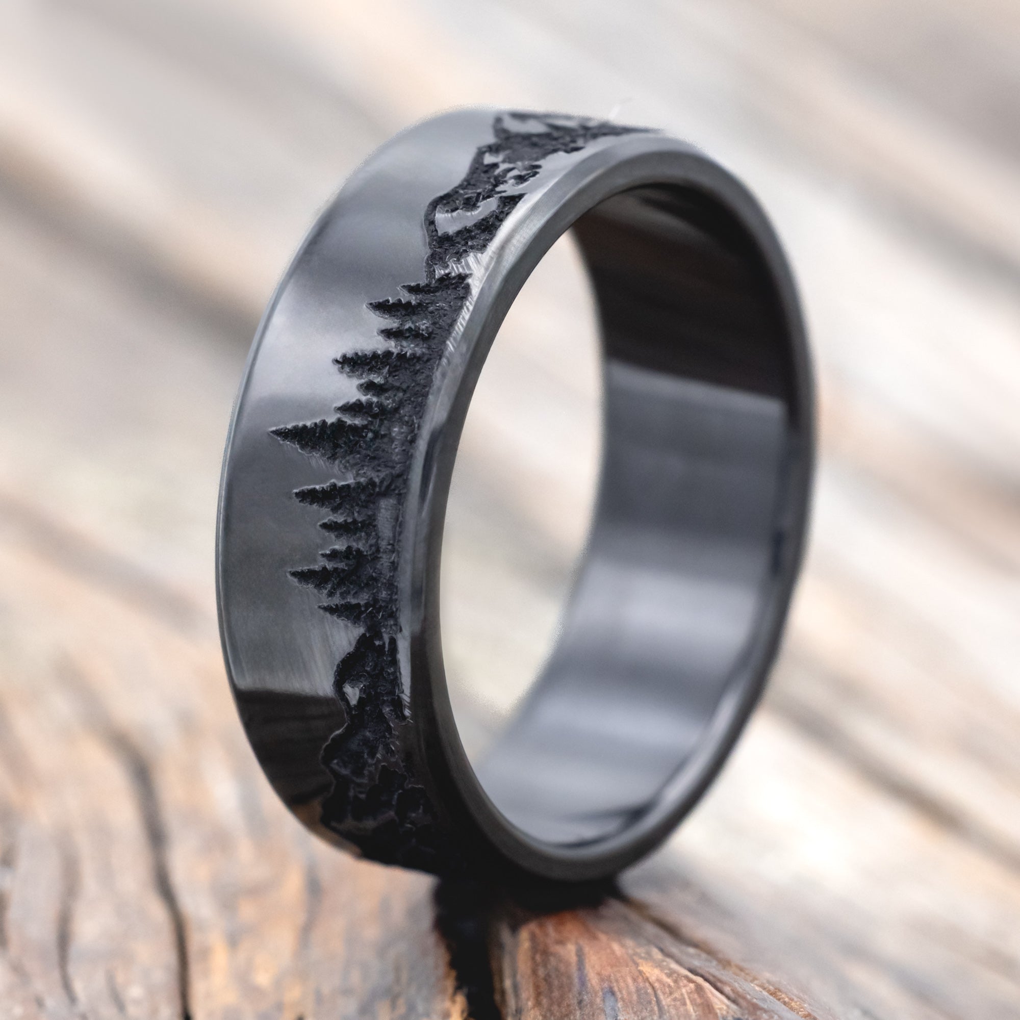 Black zirconium ring with mountain & tree engraving on a wooden surface