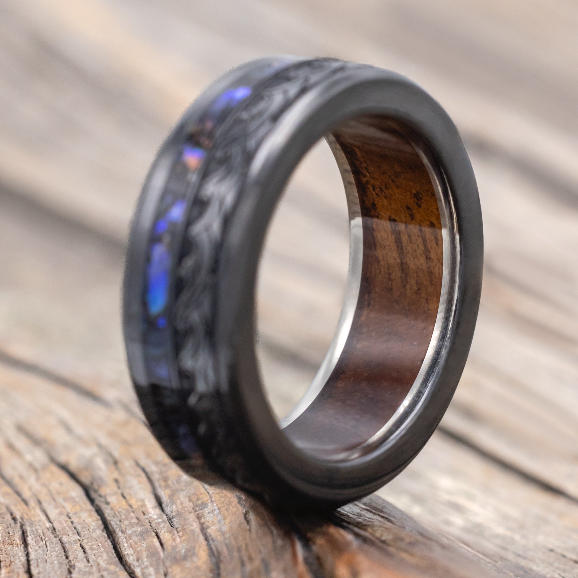 Black ring with paua shell, koa wood and wave engravings on a wooden surface