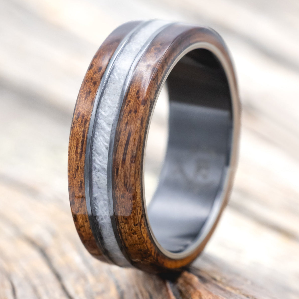 black zirconium wedding ring with koa wood and wedding dress inlay on wooden surface