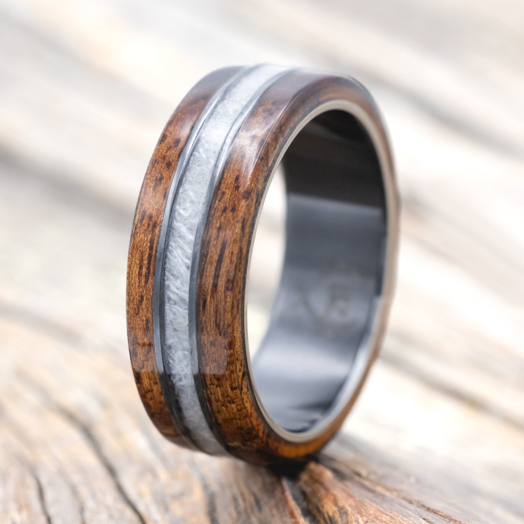 black zirconium wedding ring with koa wood and wedding dress inlay on wooden surface