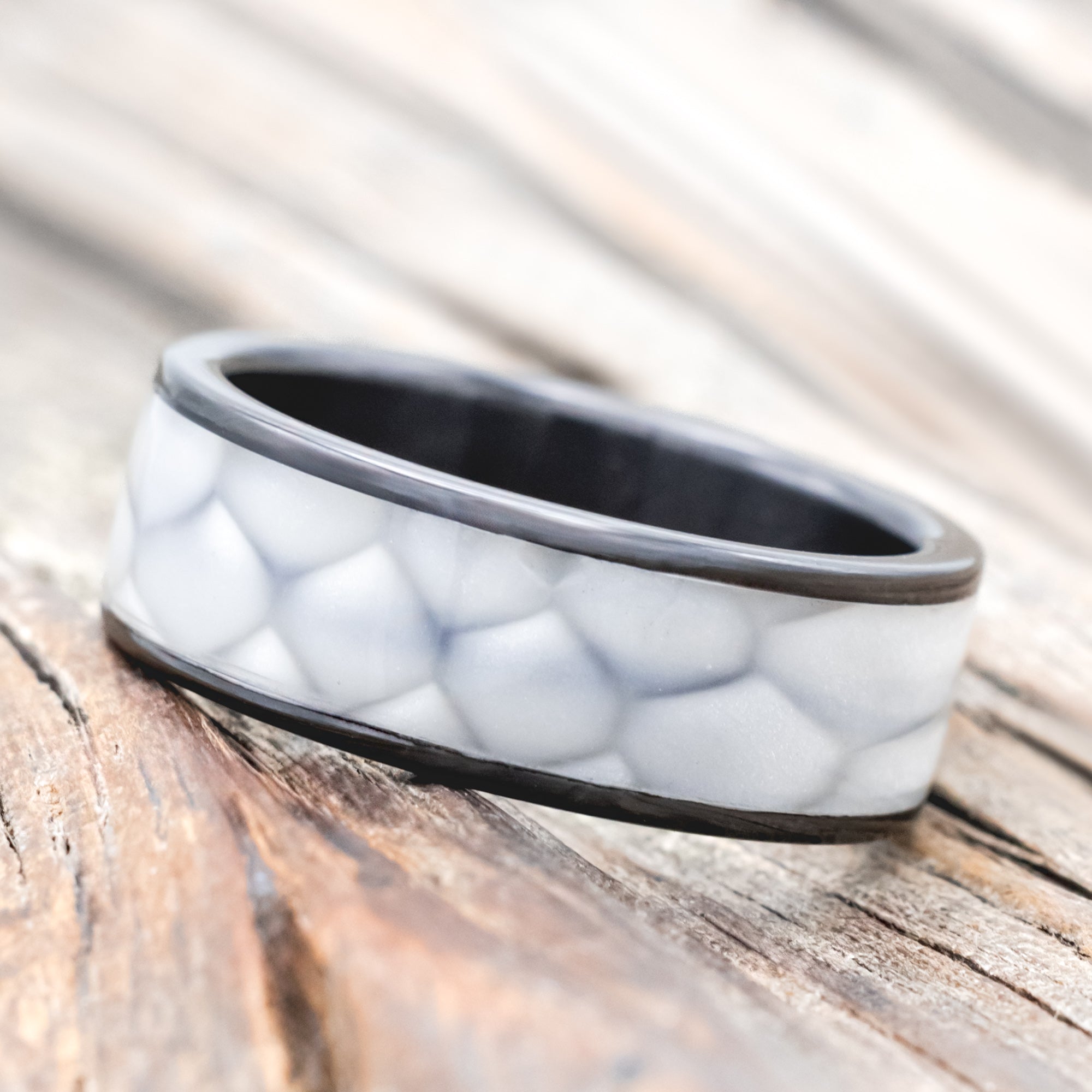 Black zirconium ring with faux white scale inlay on a wooden surface