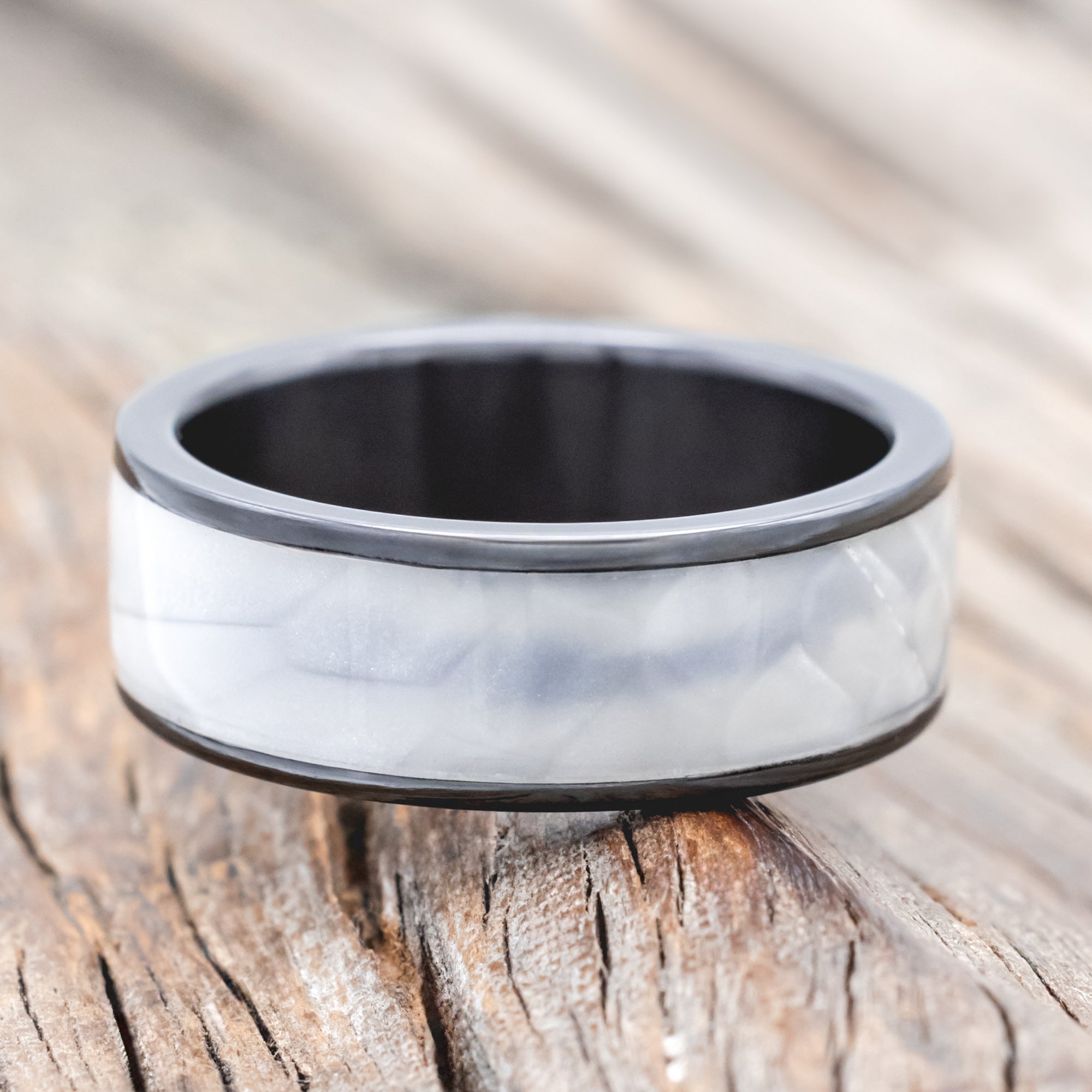 Black zirconium ring with faux white scale inlay on a wooden surface