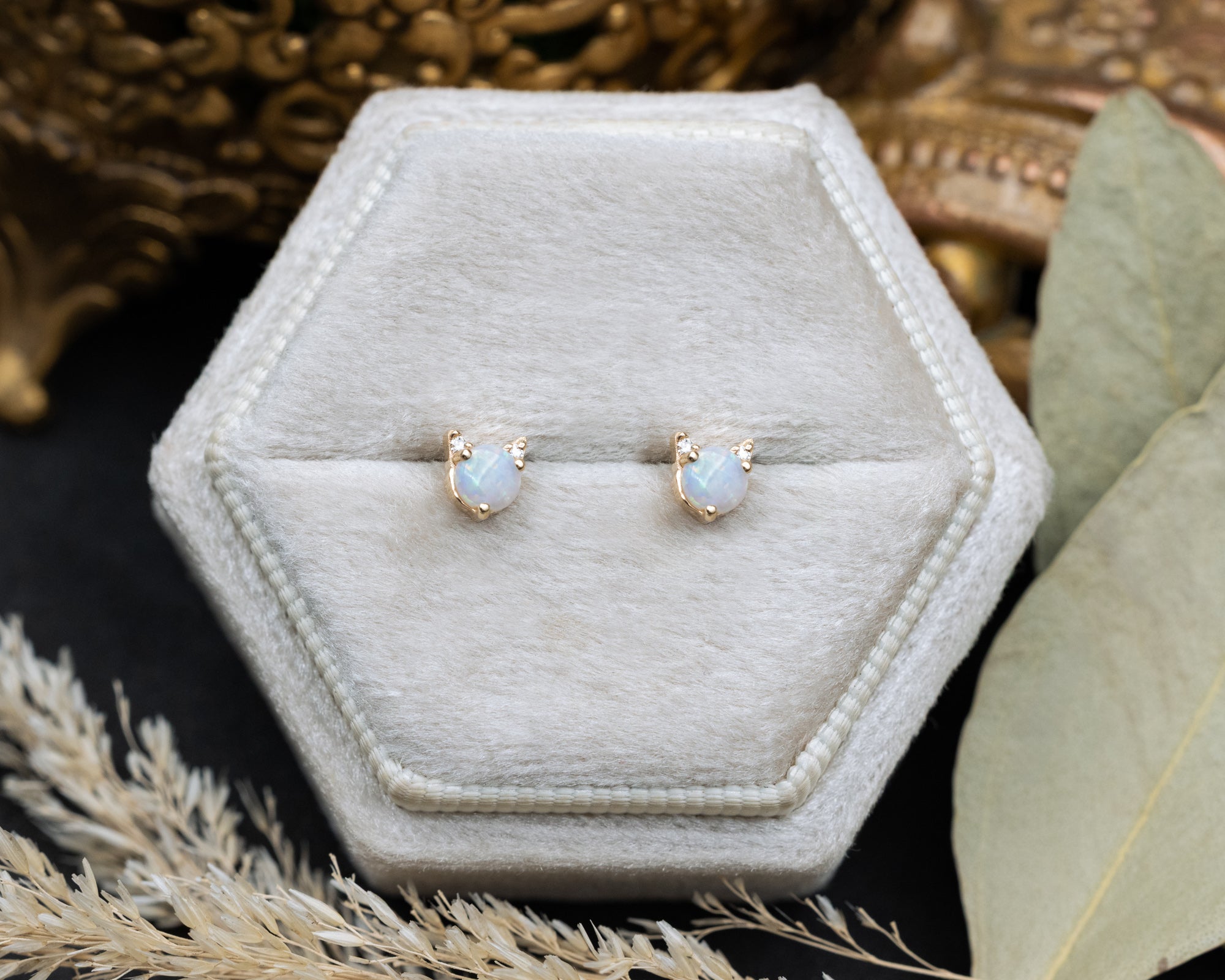 Pair of opal cat-shaped stud earrings on a white cushion against a decorative background