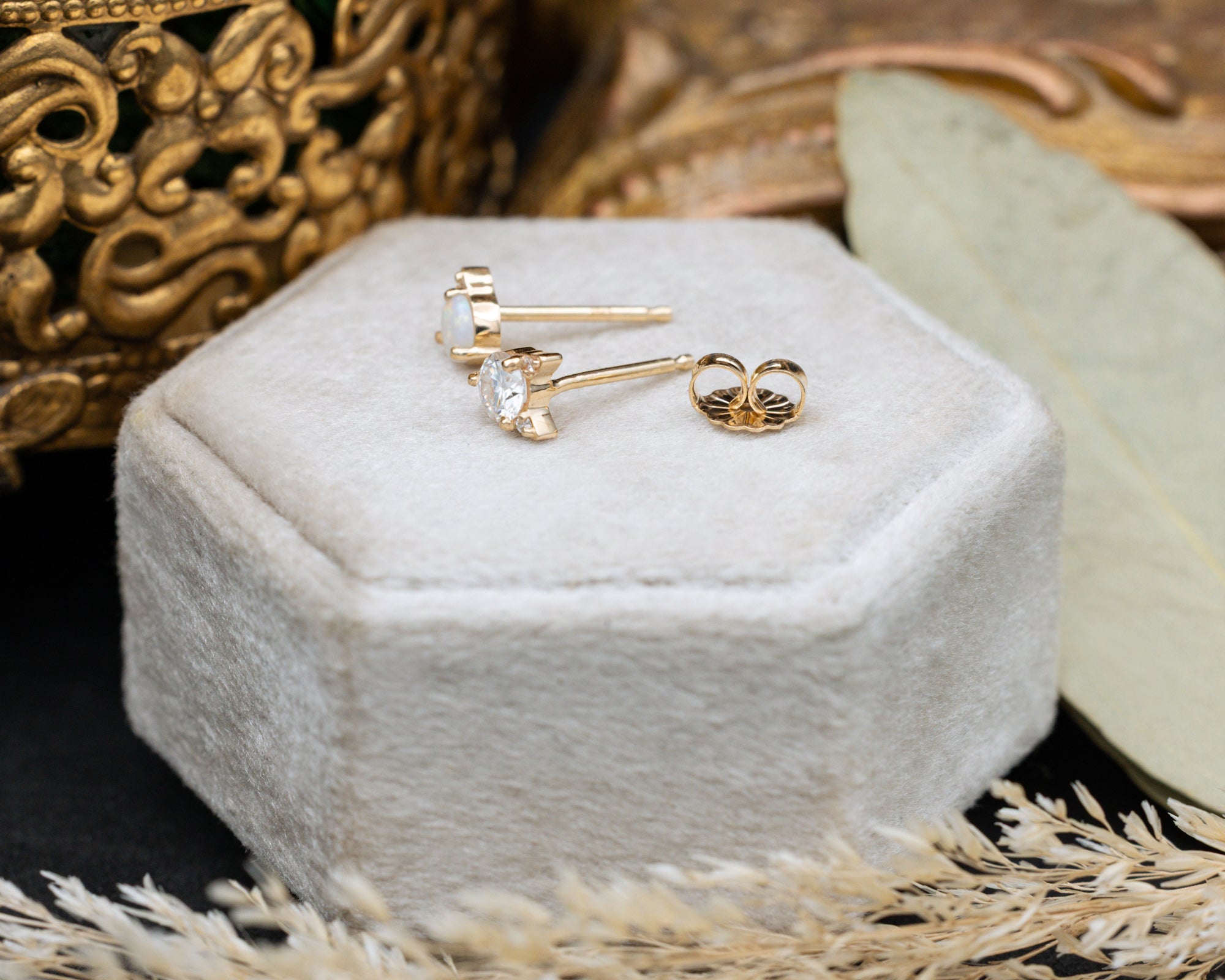 Side view of cat-shaped earrings with a posts and backs on a white cushion against a decorative background