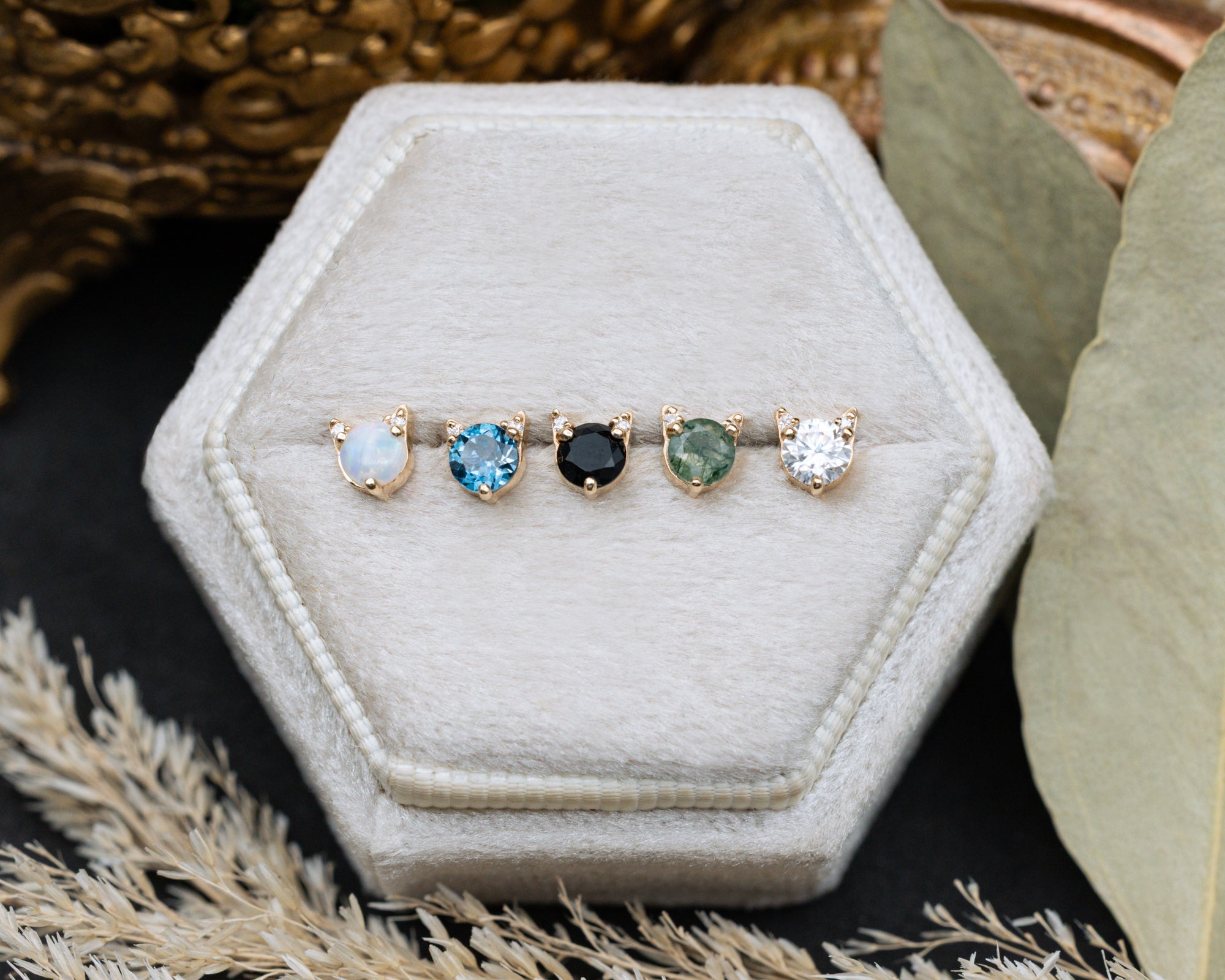 5 cat-shaped stud earrings on a white cushion against a decorative background