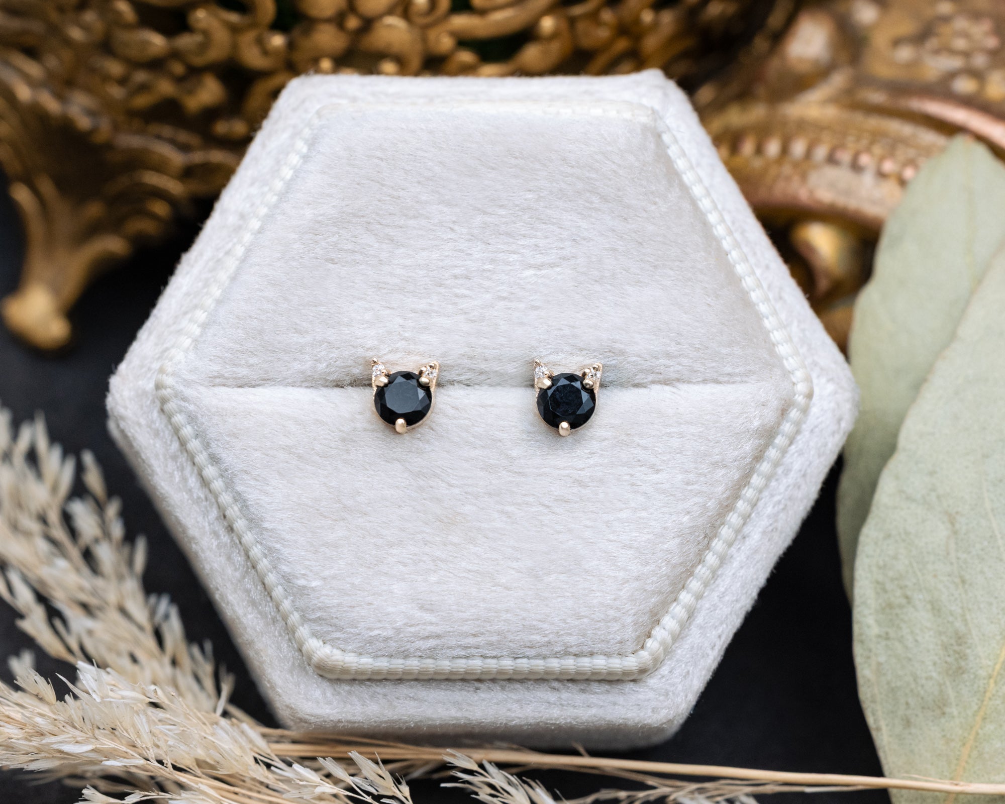 Pair of onyx cat-shaped stud earrings on a white cushion against a decorative background