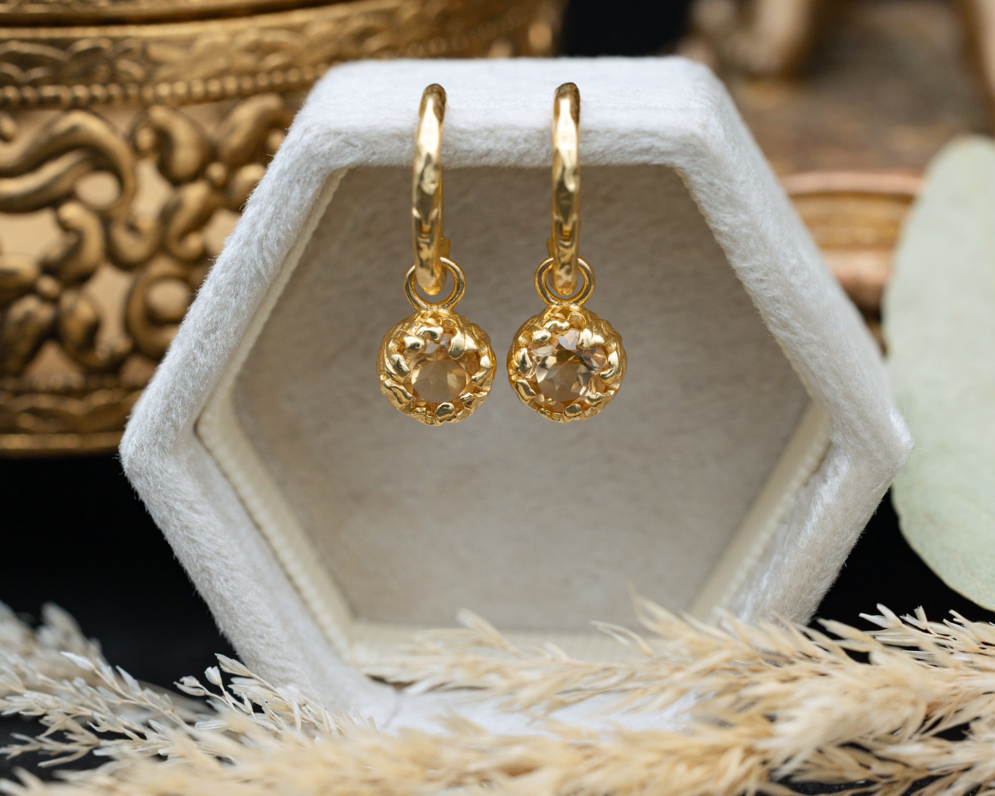 Gold citrine earrings on a white hexagonal stand with a decorative background