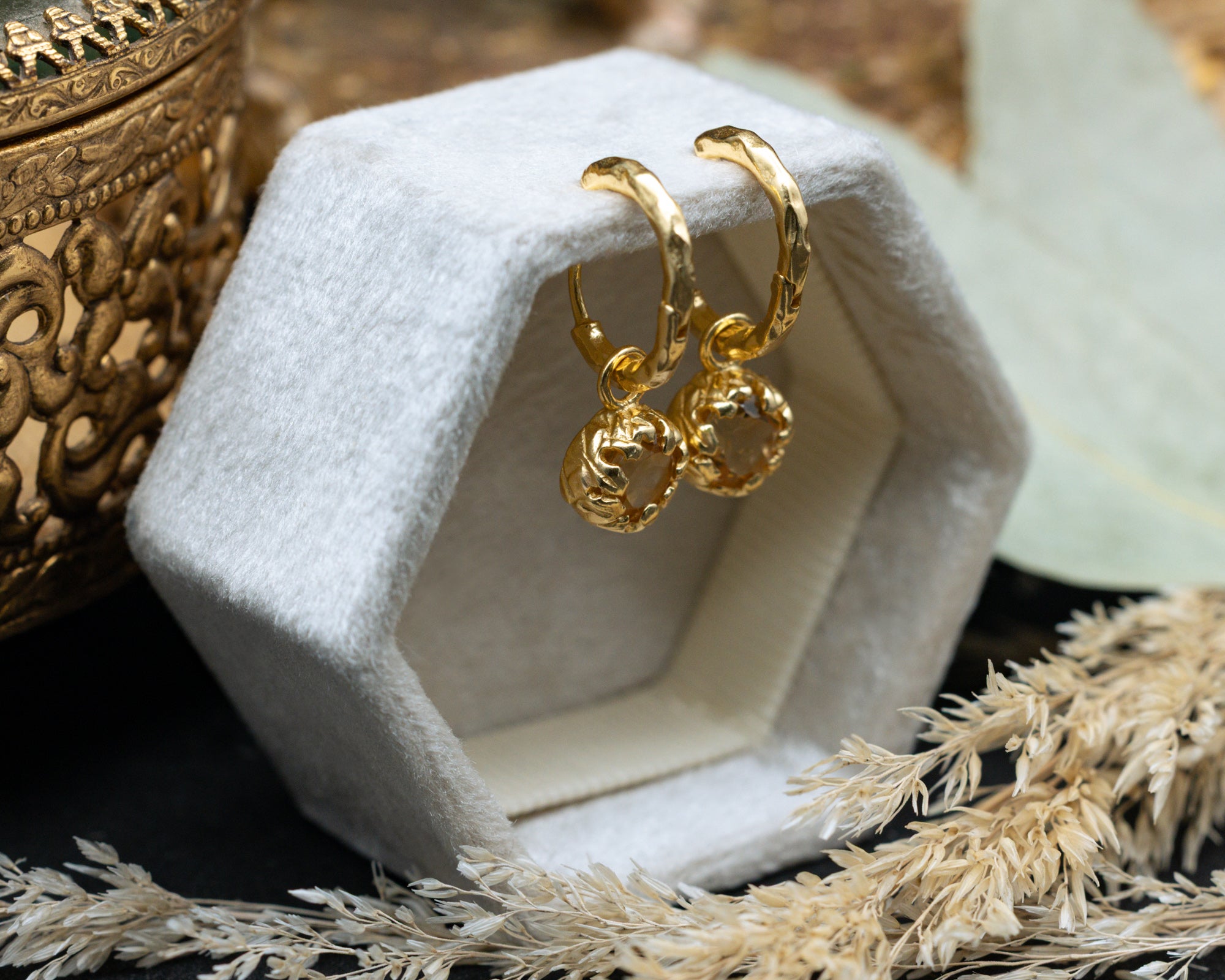 Gold citrine earrings on a white cushion with a decorative background