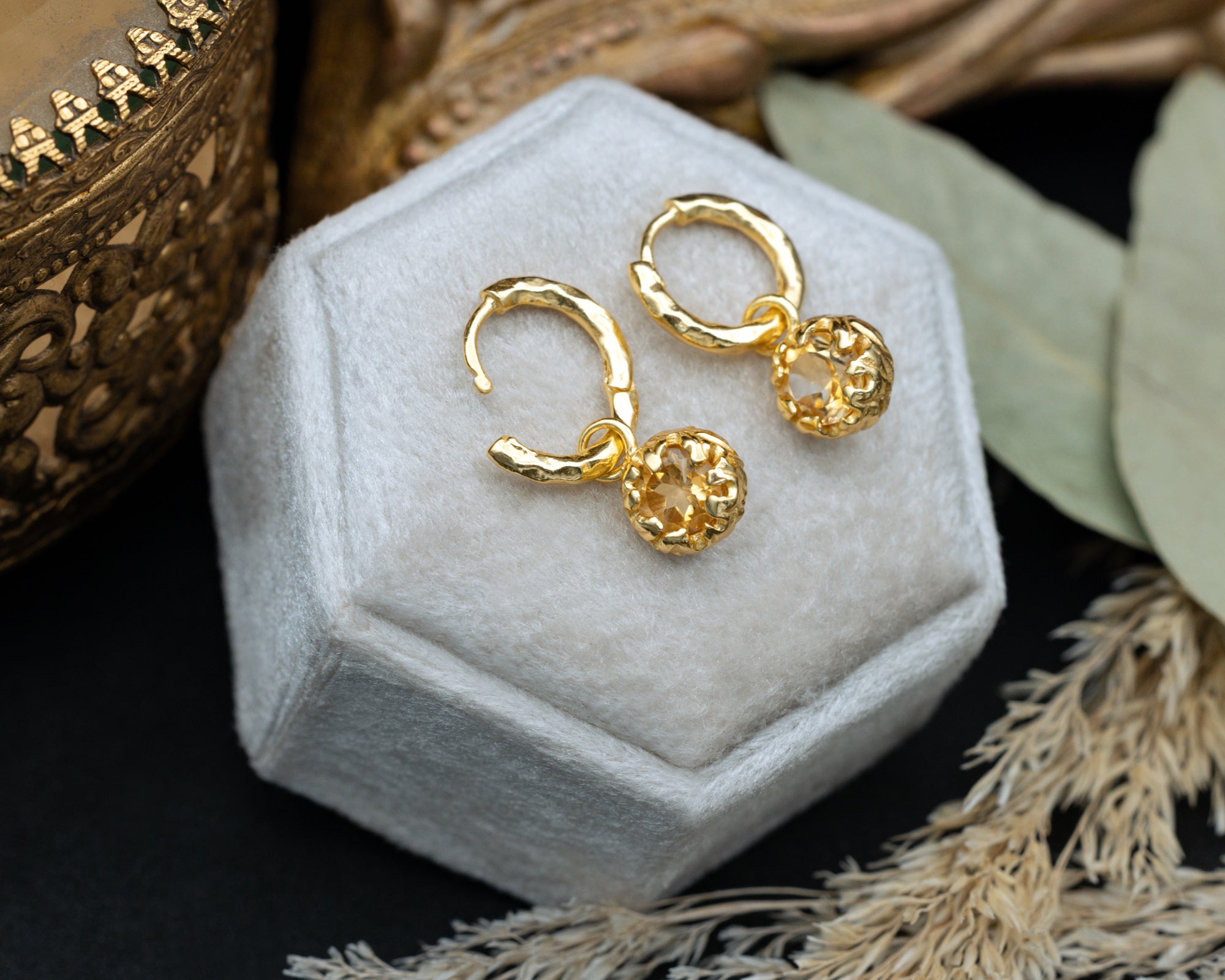 Gold citrine hoop earrings on a white hexagonal jewelry box with decorative elements.