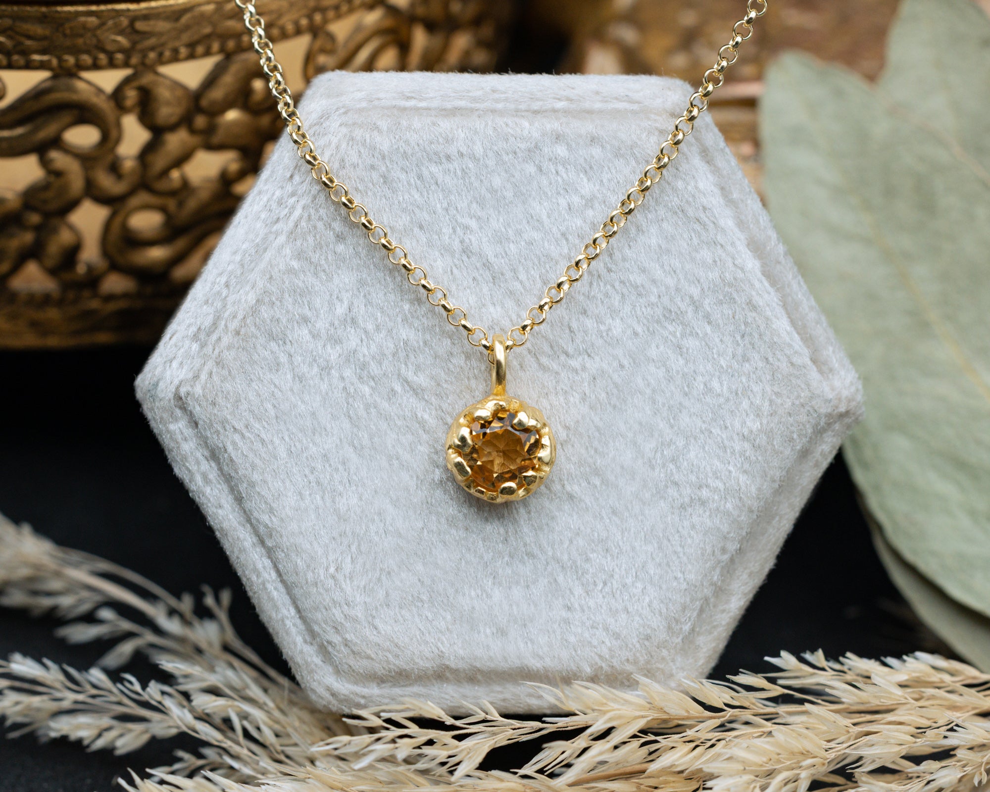 Gold necklace with a citrine pendant on a white hexagonal stand with a decorative background