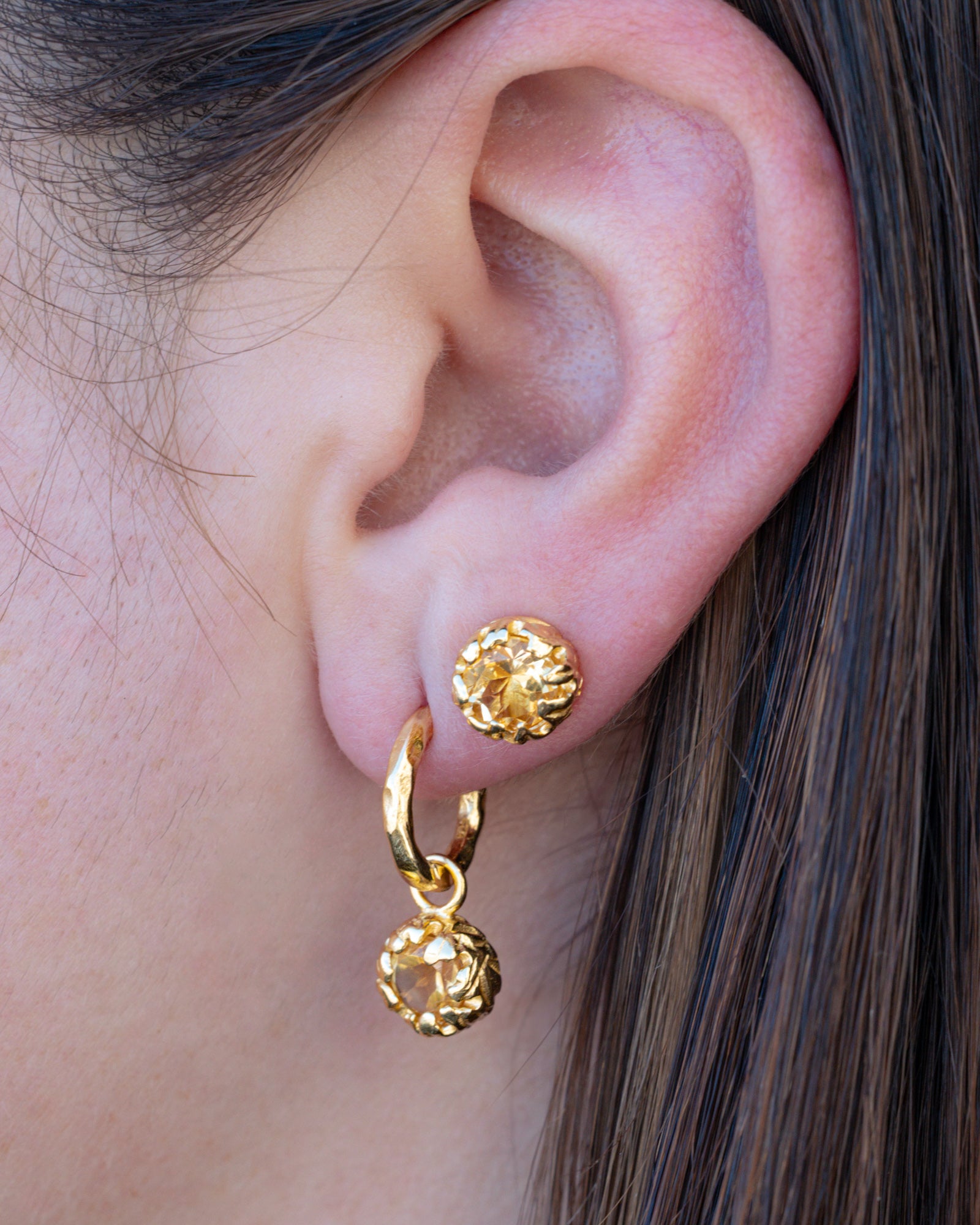 Close-up of a person wearing gold hoop earrings with citrine.