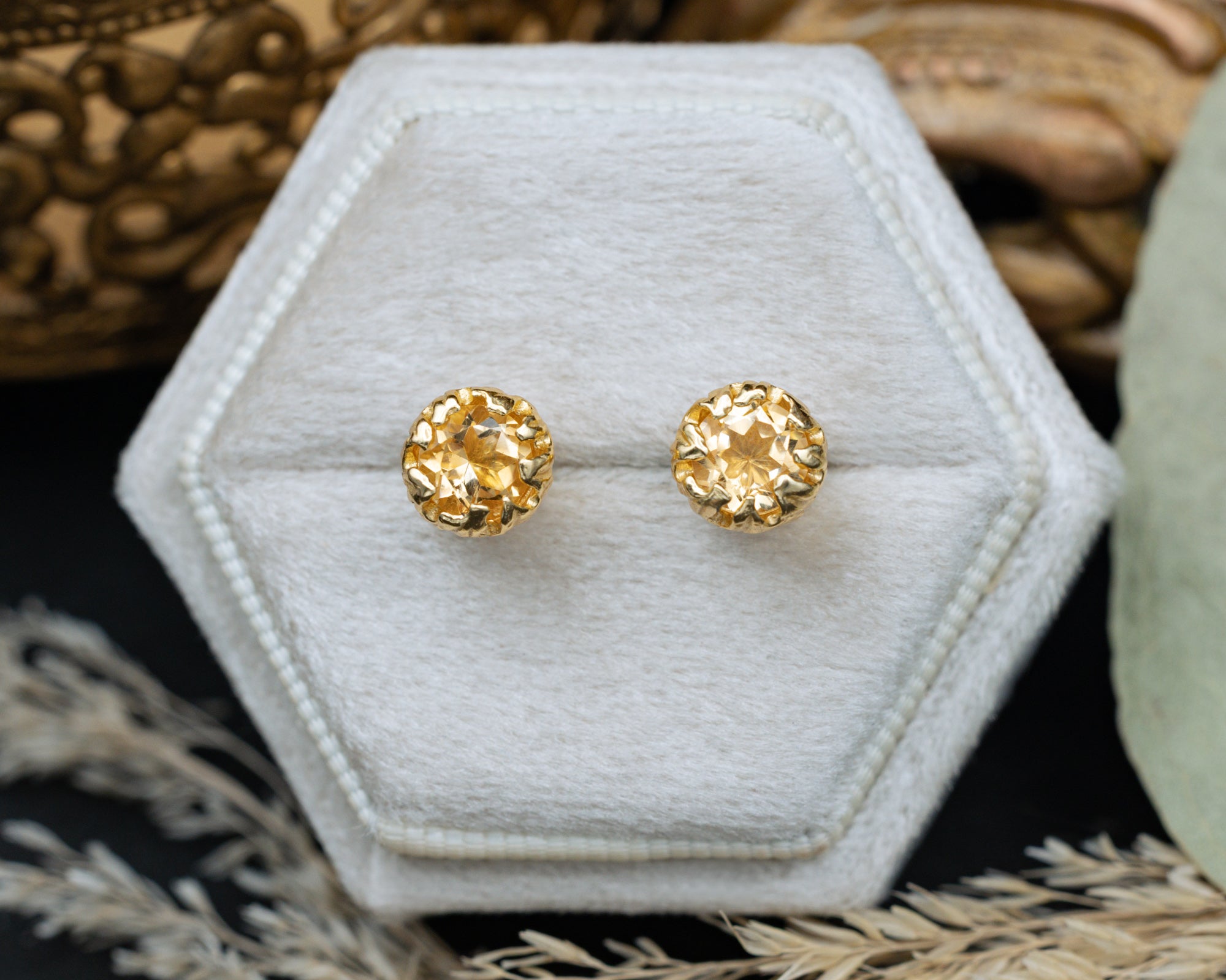 Gold citrine earrings on a white hexagonal display stand with a natural background