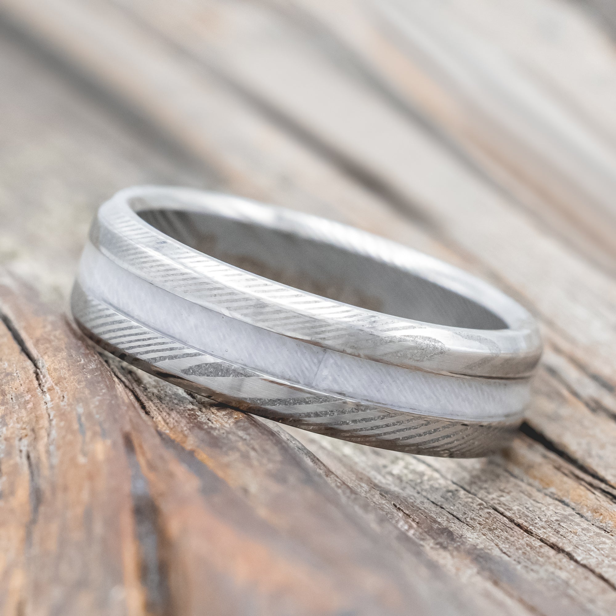 Damascus steel ring with wedding dress inlay on a wooden surface