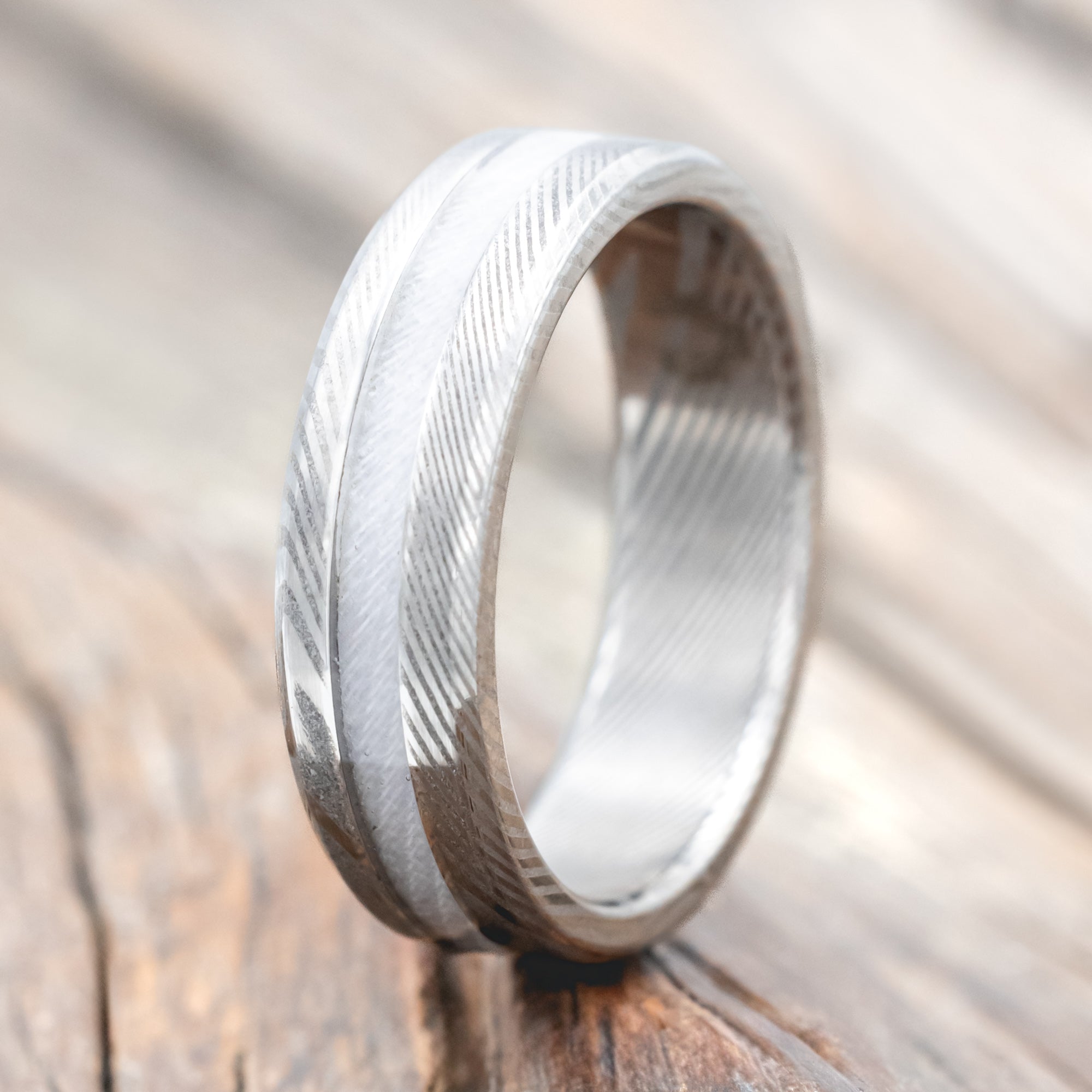 Damascus steel ring with wedding dress inlay on a wooden surface