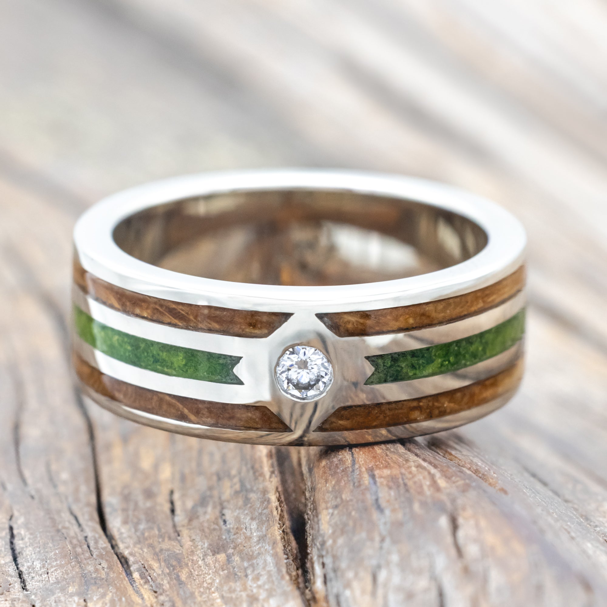 White gold ring with whiskey barrel oak and moss inlay and diamond accent on a wooden surface
